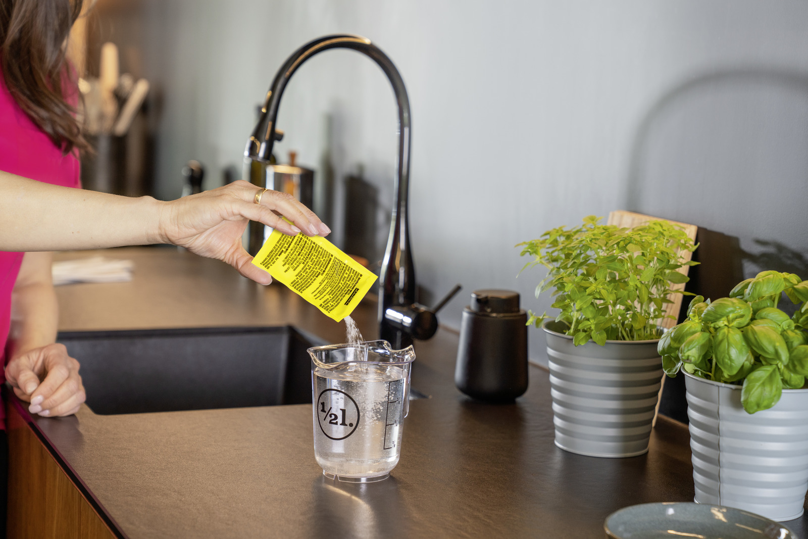 Osoba wlewa płyn z saszetki do wody w zlewce.