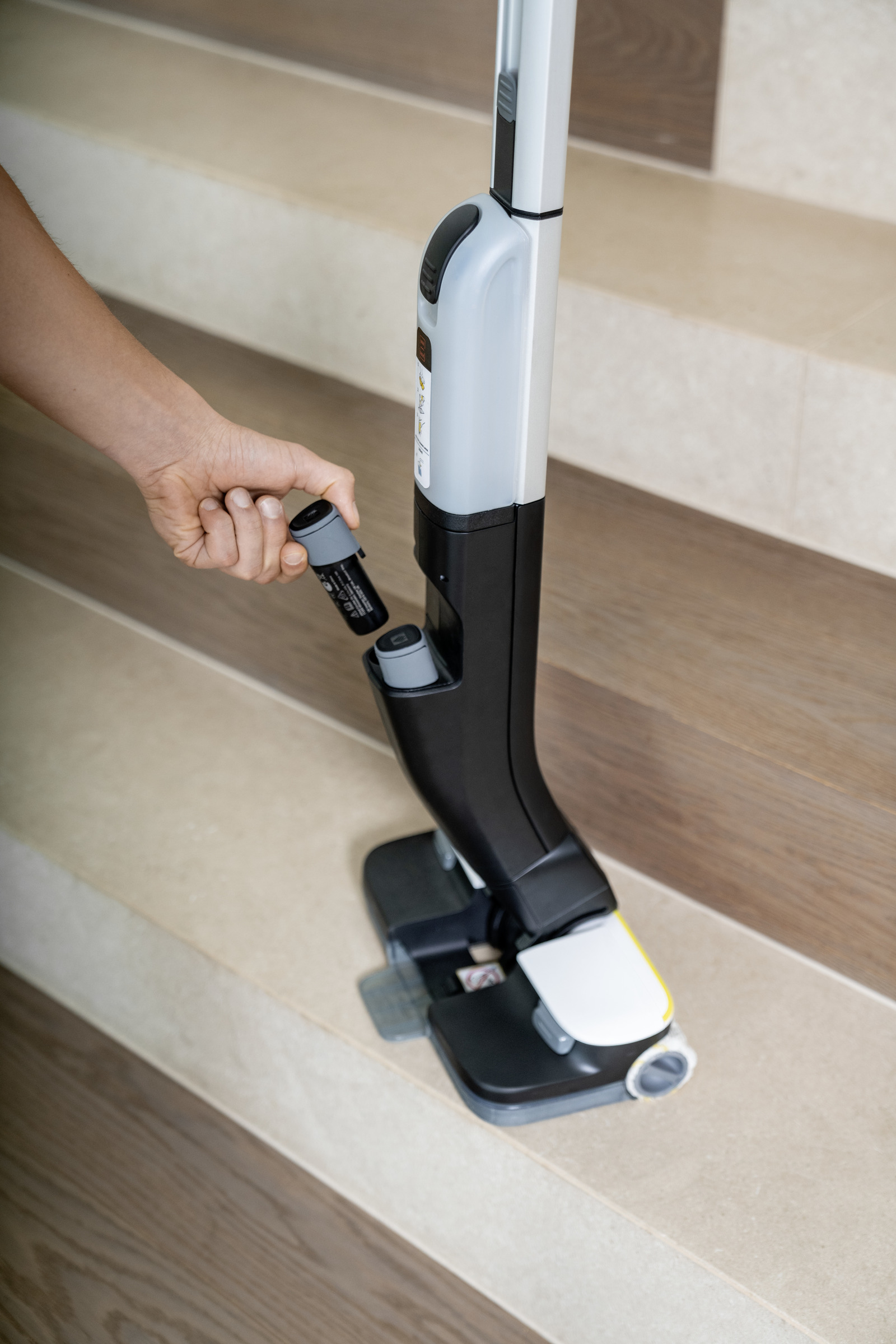 Dłoń osoby mocuje czarny element do srebrno-czarnego odkurzacza.