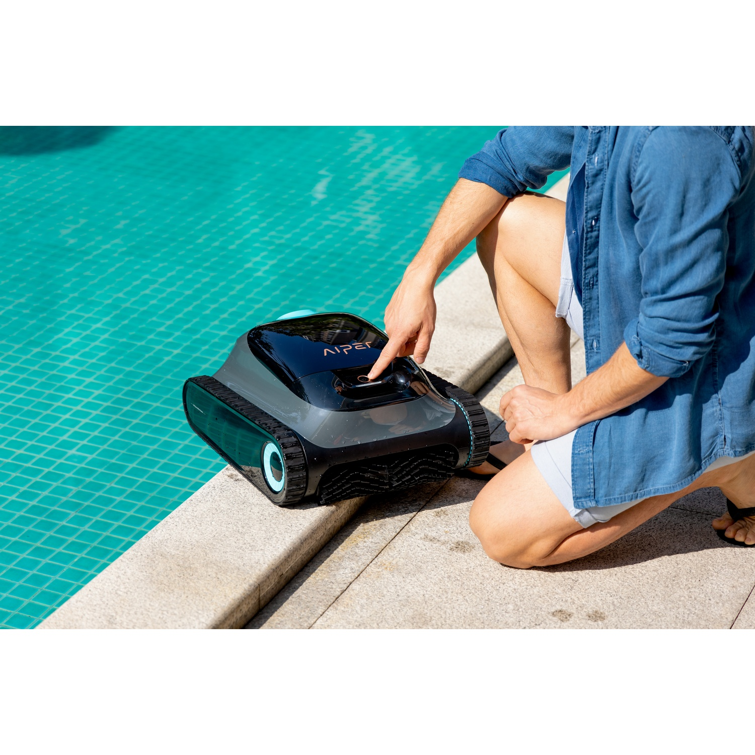 Un uomo si inginocchia in piscina con un pulitore per piscina nero e grigio.