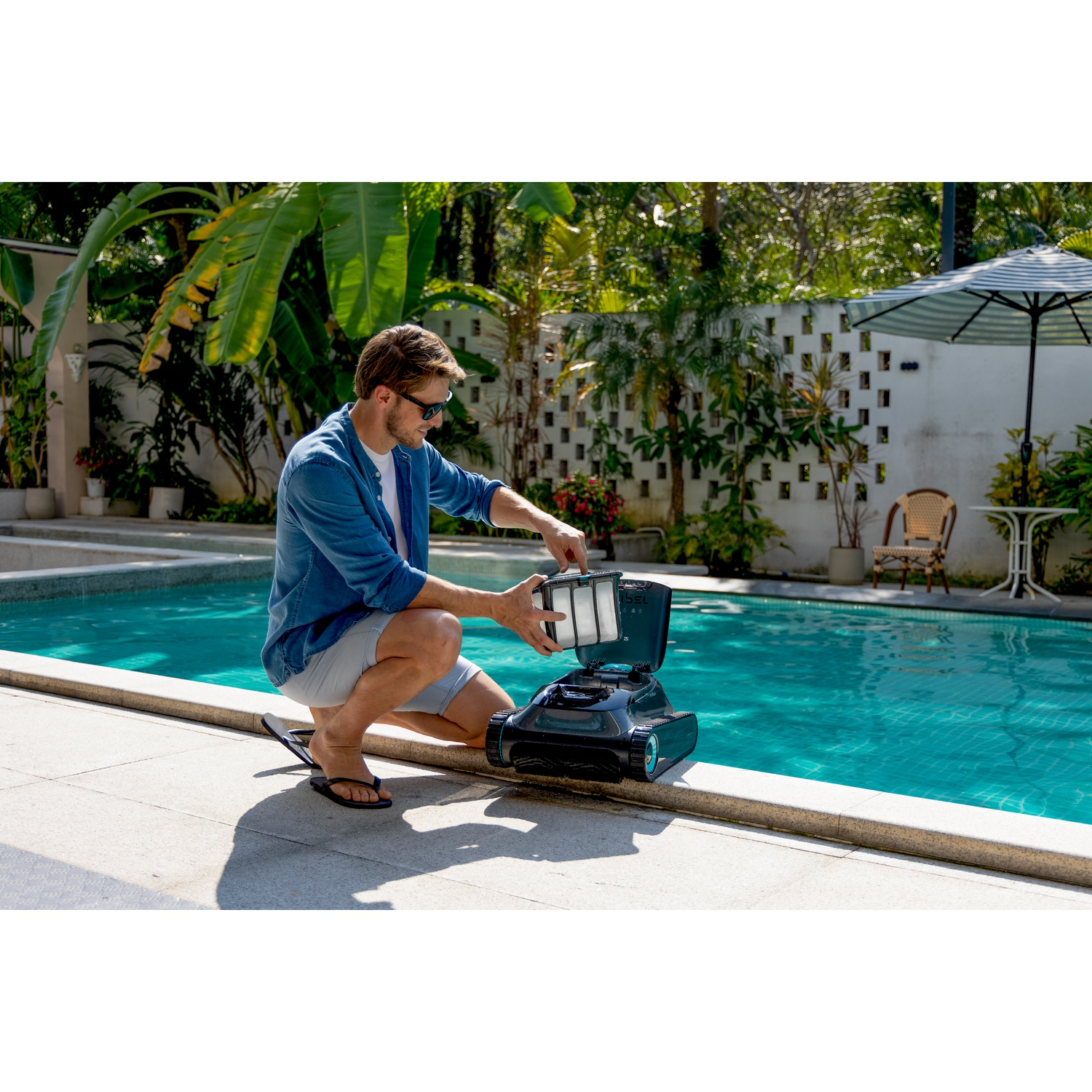 Uomo vicino alla piscina con pulitore. Piante verdi e acqua sullo sfondo.