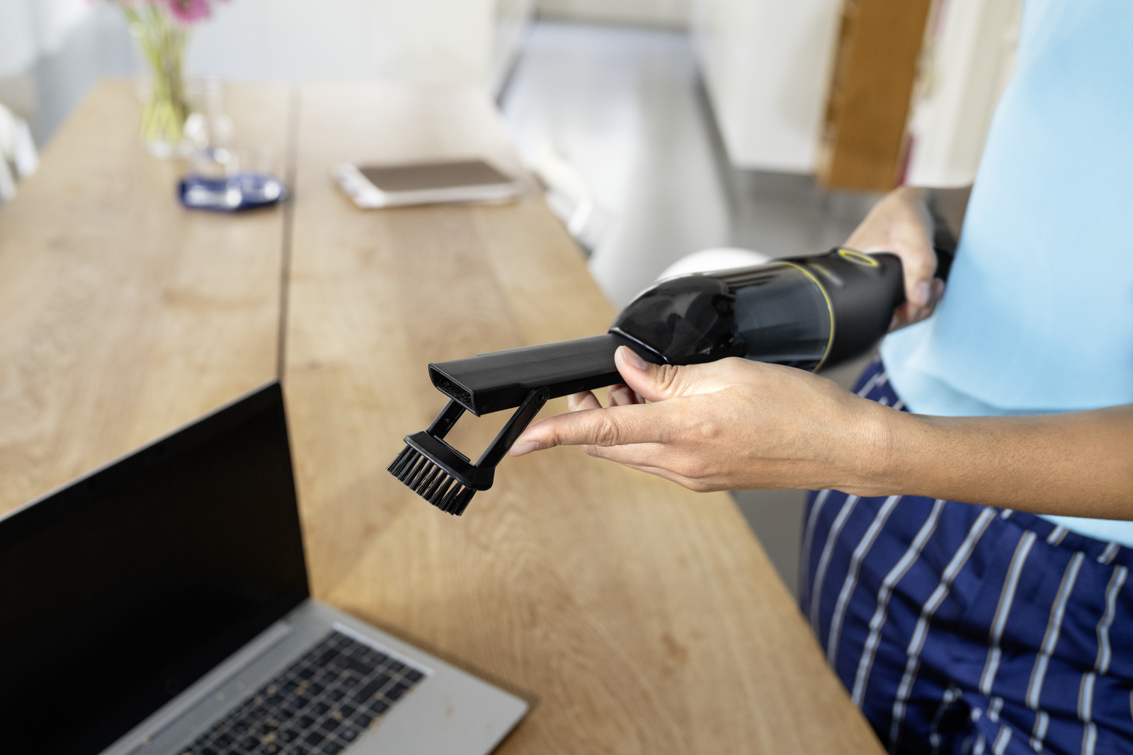Osoba trzymająca czarno-złoty odkurzacz ręczny, w pobliżu laptopa i stołu.