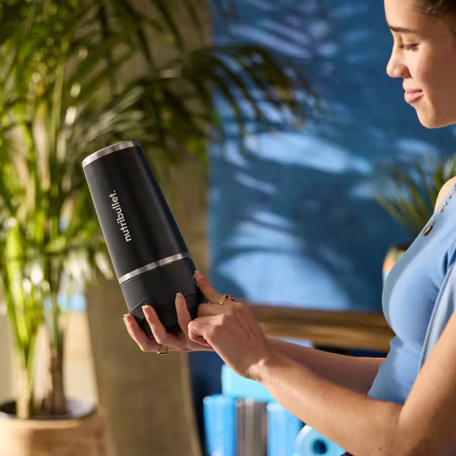 Donna che usa un Nutribullet nero, tenendolo con una mano, in un ambiente luminoso.