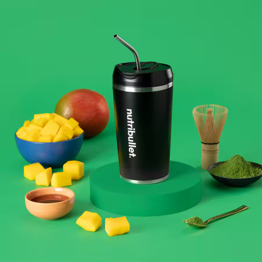 Bicchiere nero con cannuccia, mango, cubetti di mango in ciotola, matcha, cucchiaio e frusta.