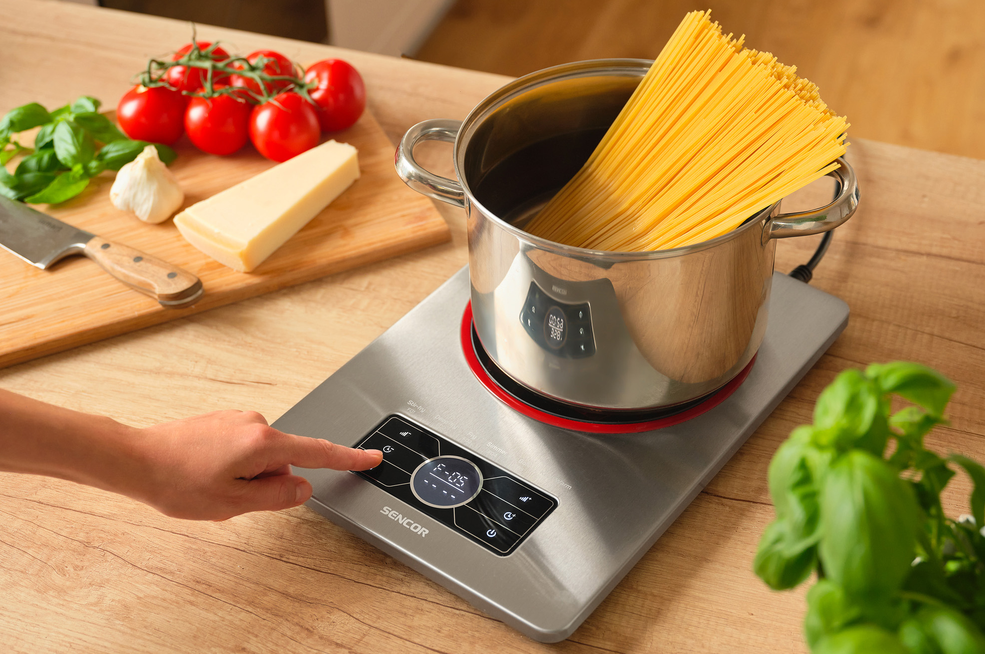 Személy gombot nyom egy főzőkészüléken. Spagetti van egy fazékban a készüléken.