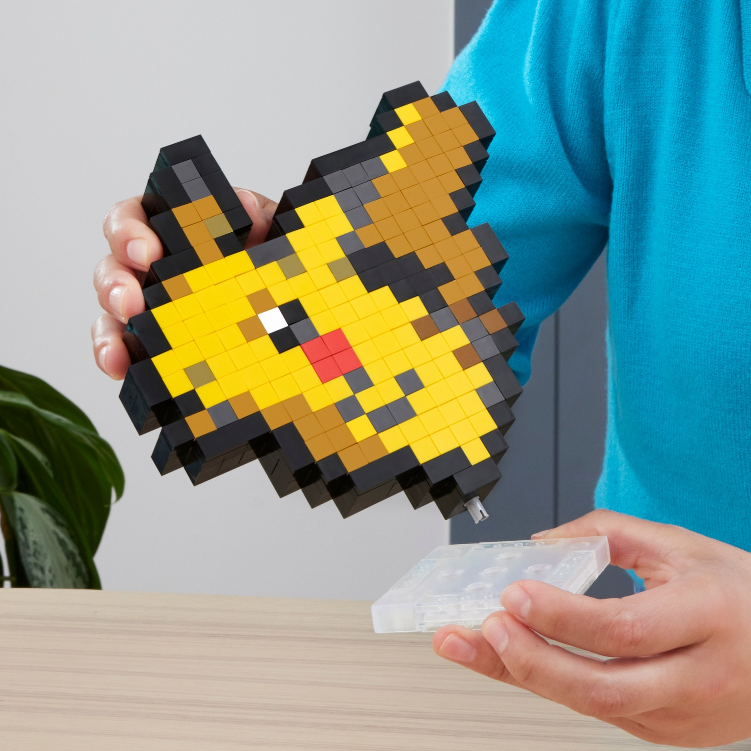 Una persona tiene in mano un Pikachu pixelato fatto di blocchi, con una base trasparente sotto.