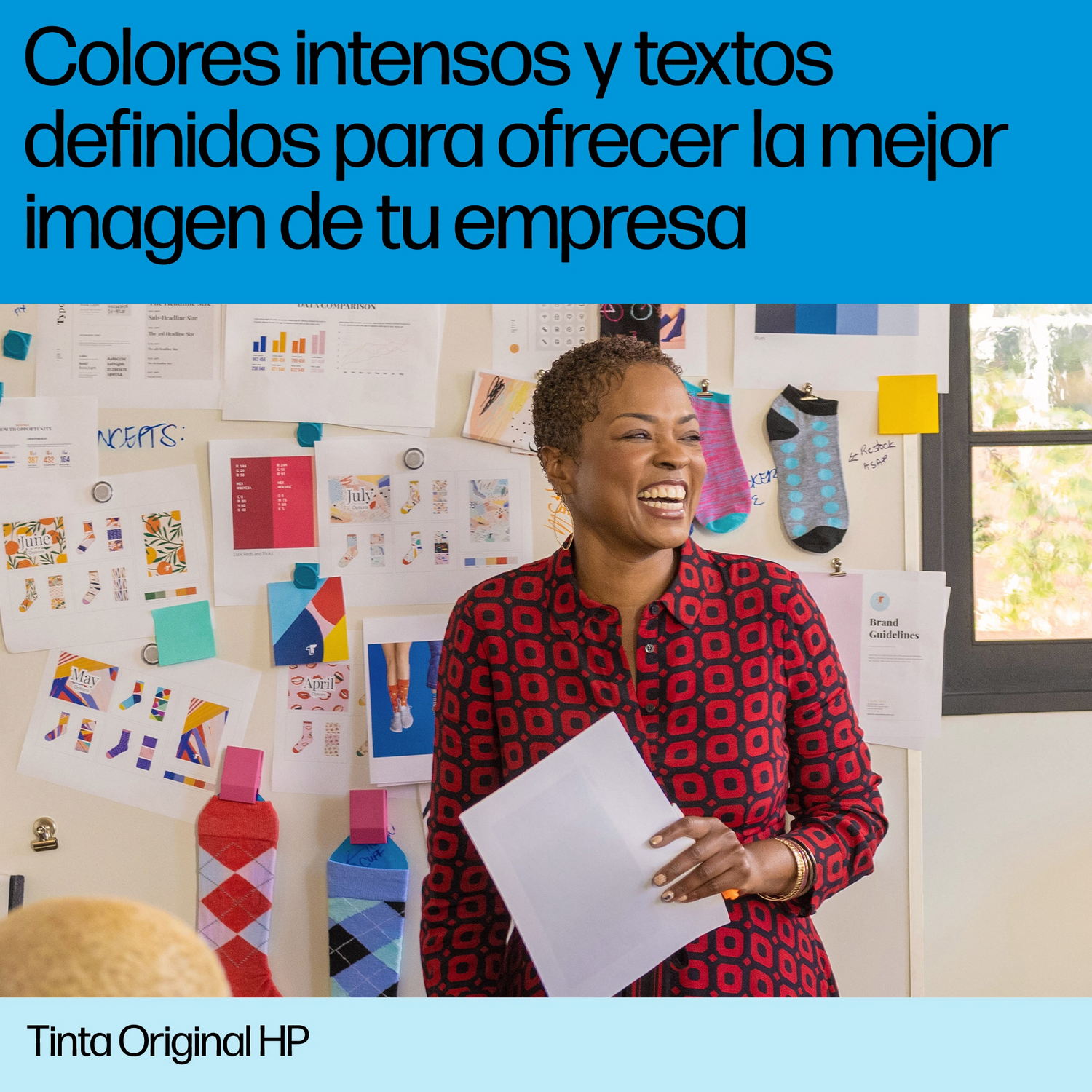 Una mujer sonríe mientras sostiene un papel frente a una pared colorida con texto.