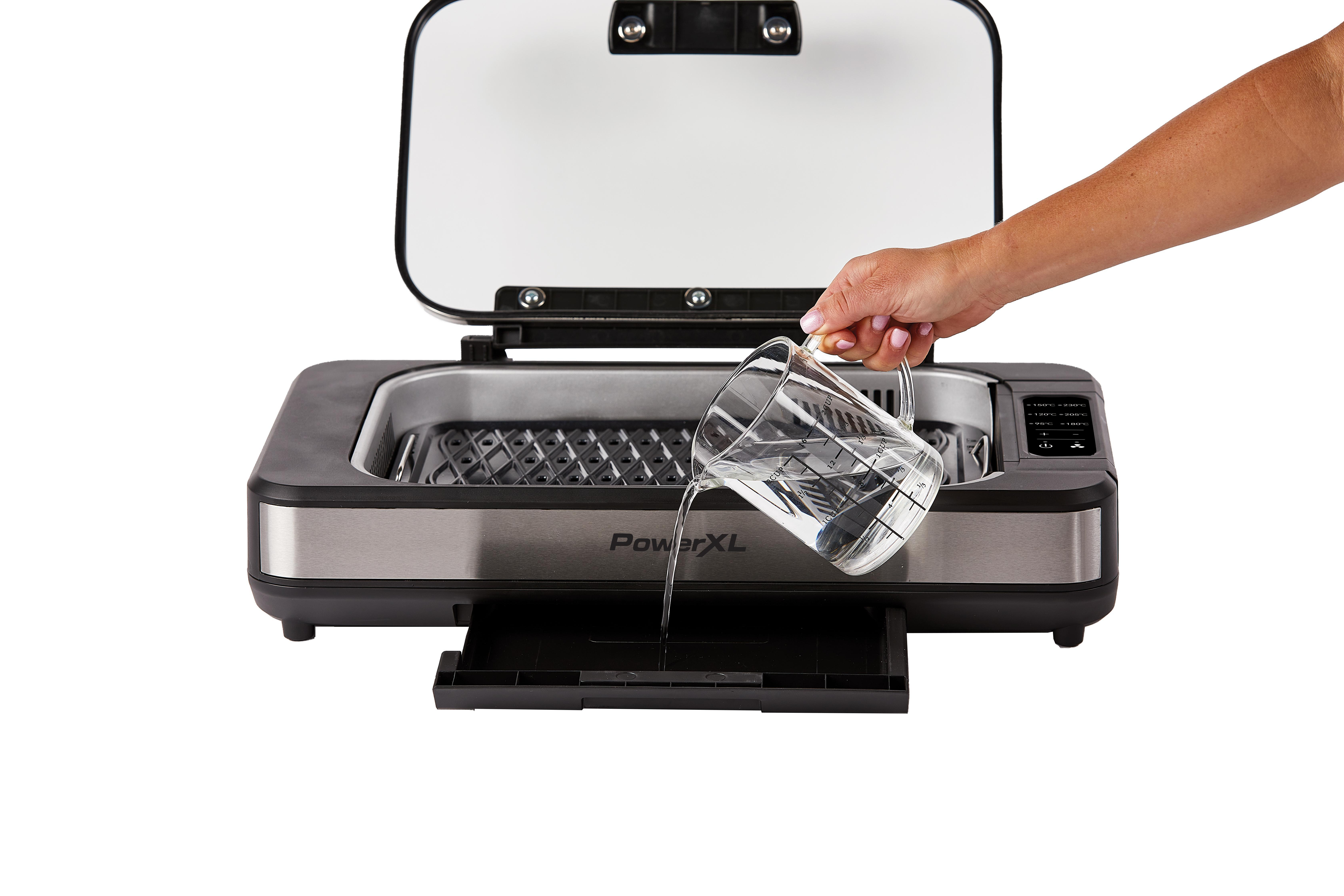 Eine Person gießt Wasser in einen Grill. Der Grill ist offen und auf weißem Hintergrund.