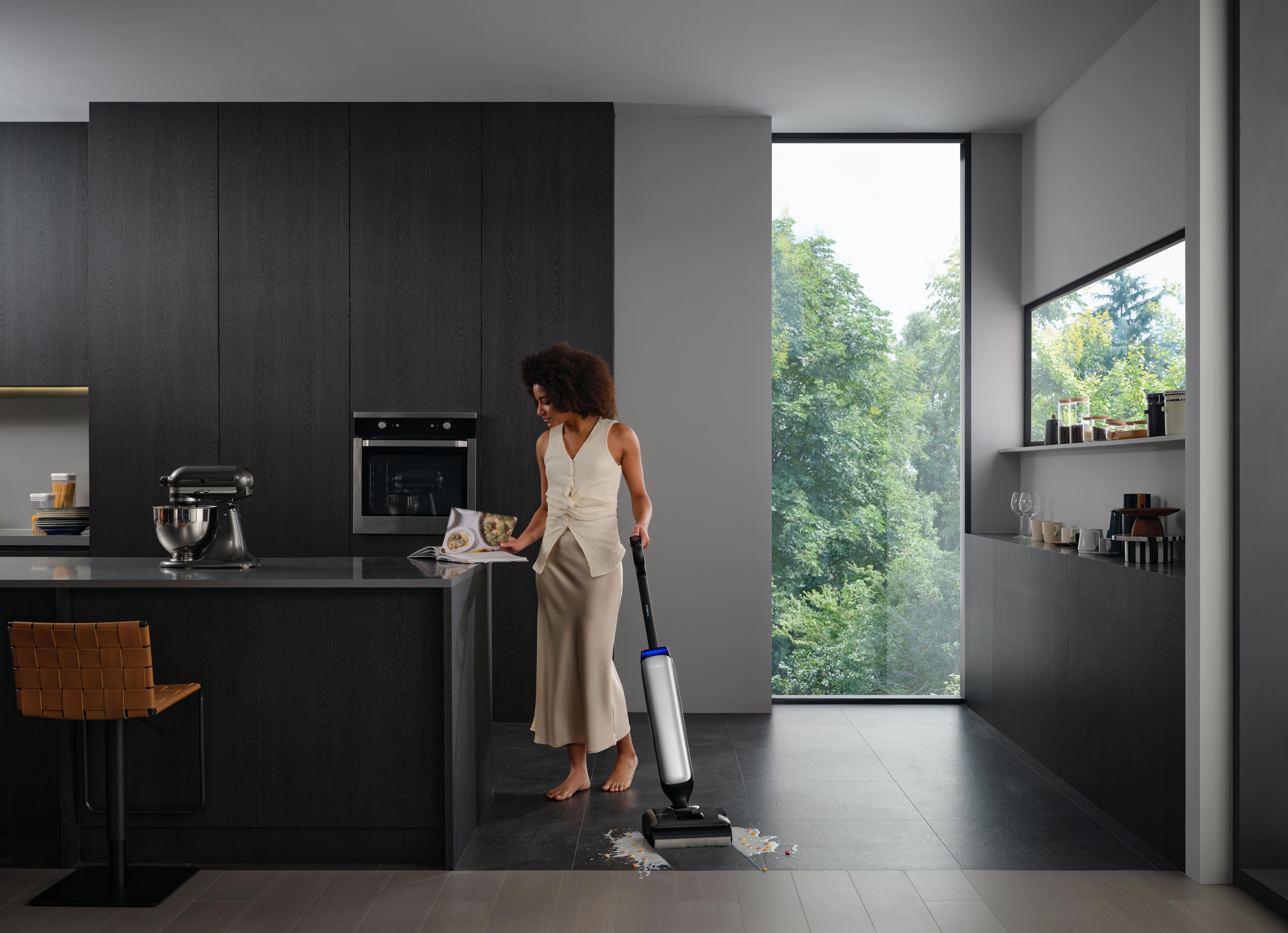 Eine Frau wischt eine verschüttete Flüssigkeit in einer modernen Küche mit dunklen Schränken auf.