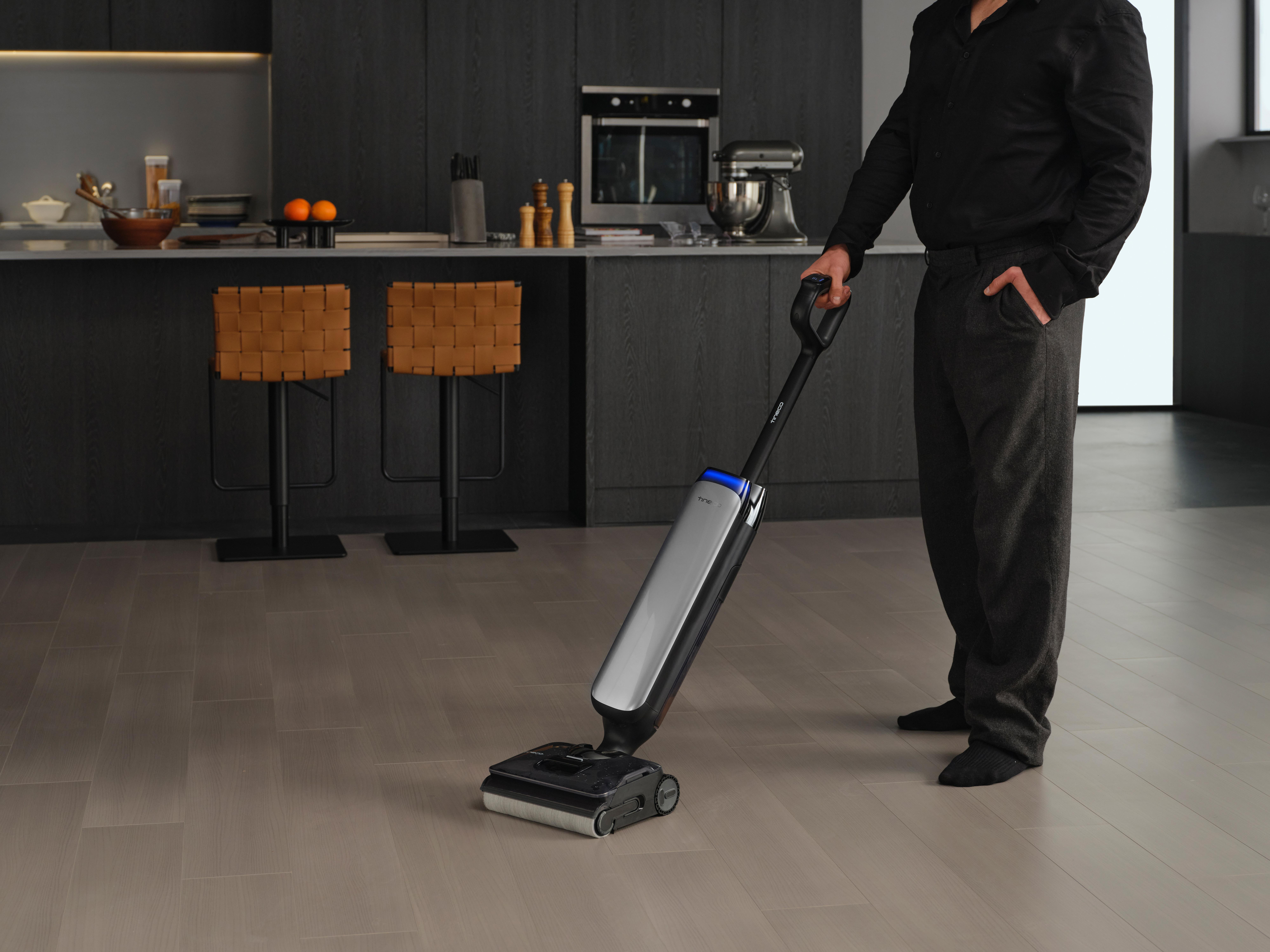 Ein Mann saugt den Boden einer modernen Küche mit einem silbernen Staubsauger.