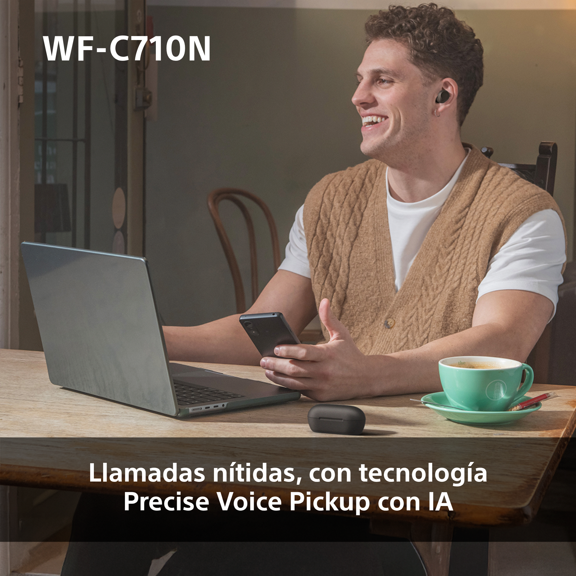 Un hombre con auriculares usando una laptop, con un teléfono y una taza de café cerca.