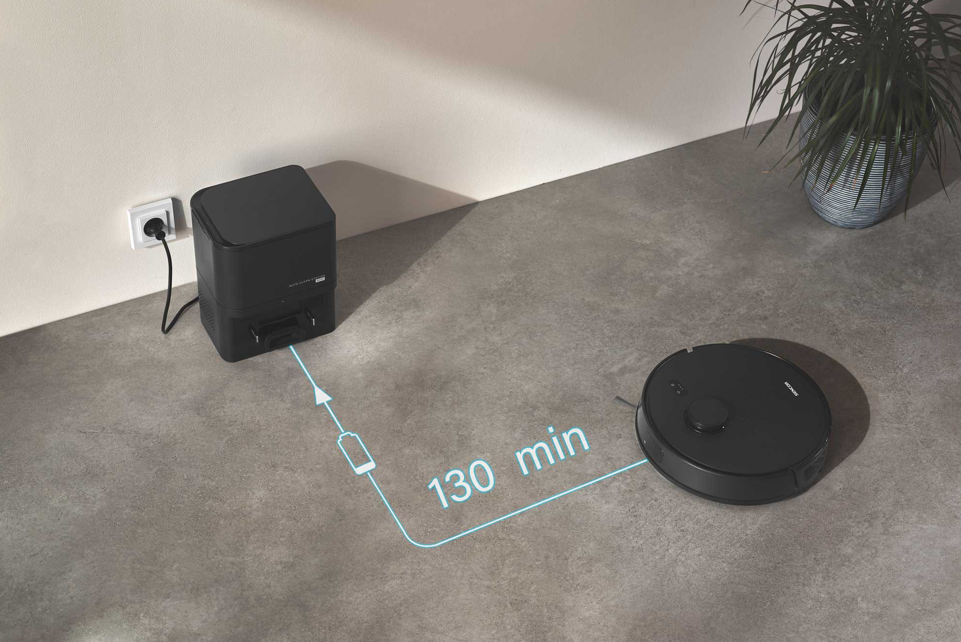 Egy fekete robotporszívó töltődik egy helyiségben egy töltőállomás mellett. Becsült idő: 130 perc.