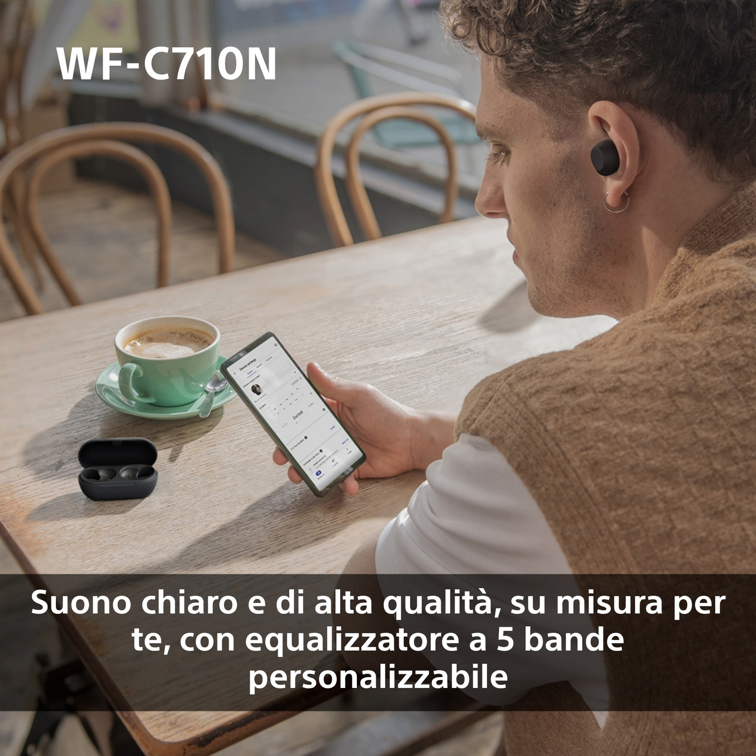 Uomo che usa il telefono con auricolari, tazza di caffè sul tavolo.