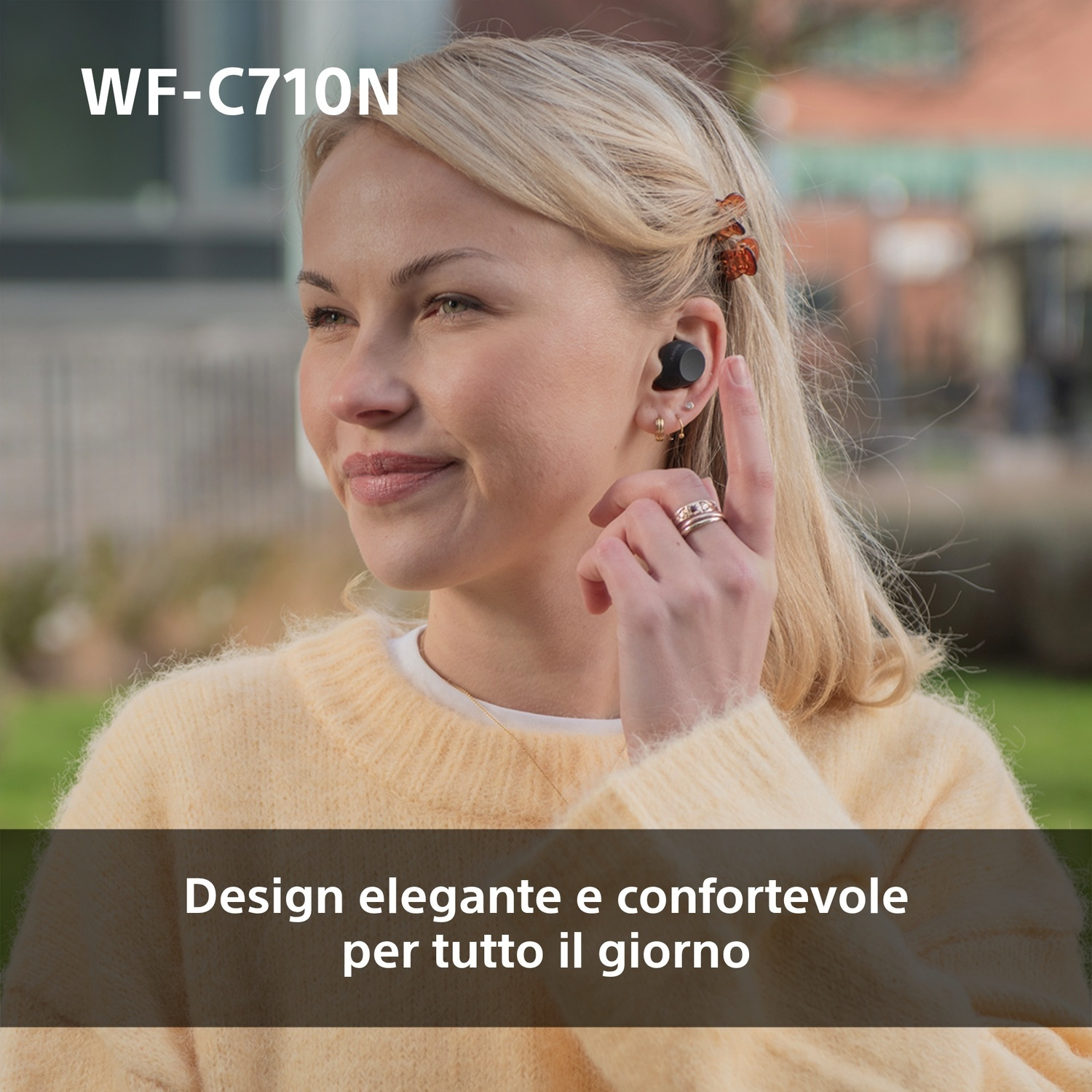 Una donna con auricolari. Ha i capelli biondi e indossa un maglione giallo.