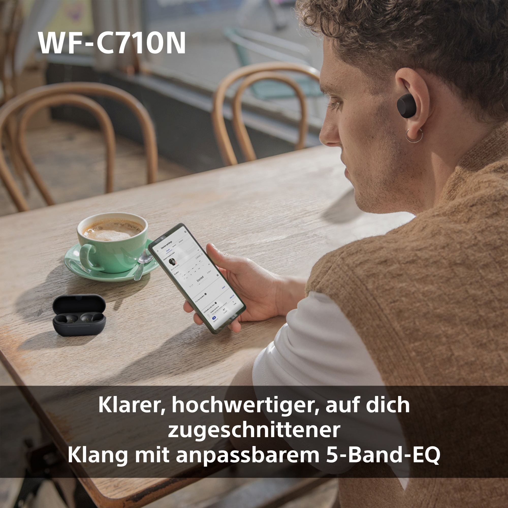 Ein Mann sitzt an einem Tisch und benutzt Ohrhörer und ein Telefon.