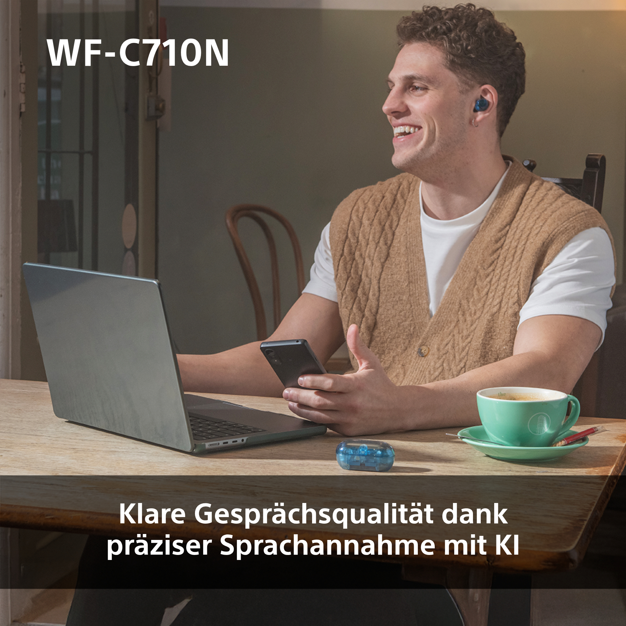 Ein Mann benutzt einen Laptop, lächelt, trägt Ohrhörer und hält ein Telefon.