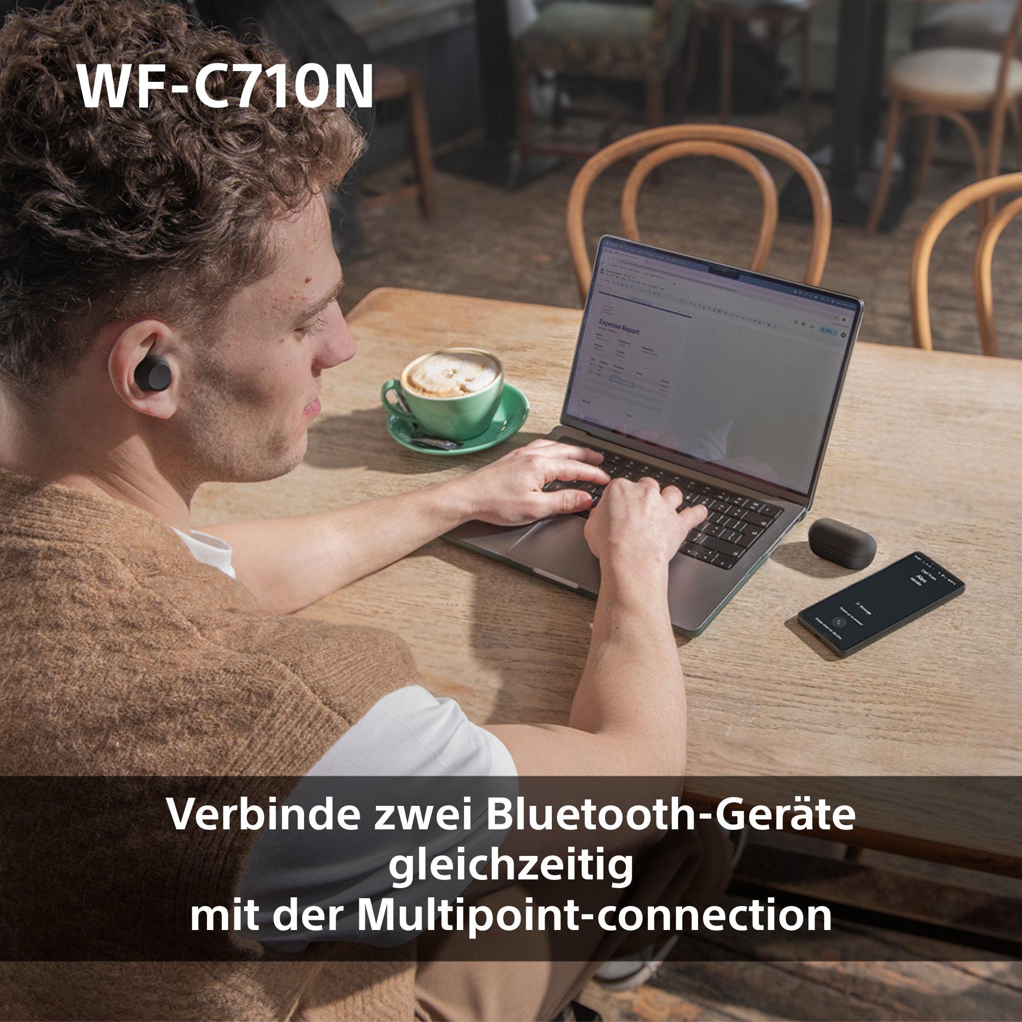 Mann benutzt Laptop mit Ohrhörern, Kaffee und Telefon auf dem Tisch.