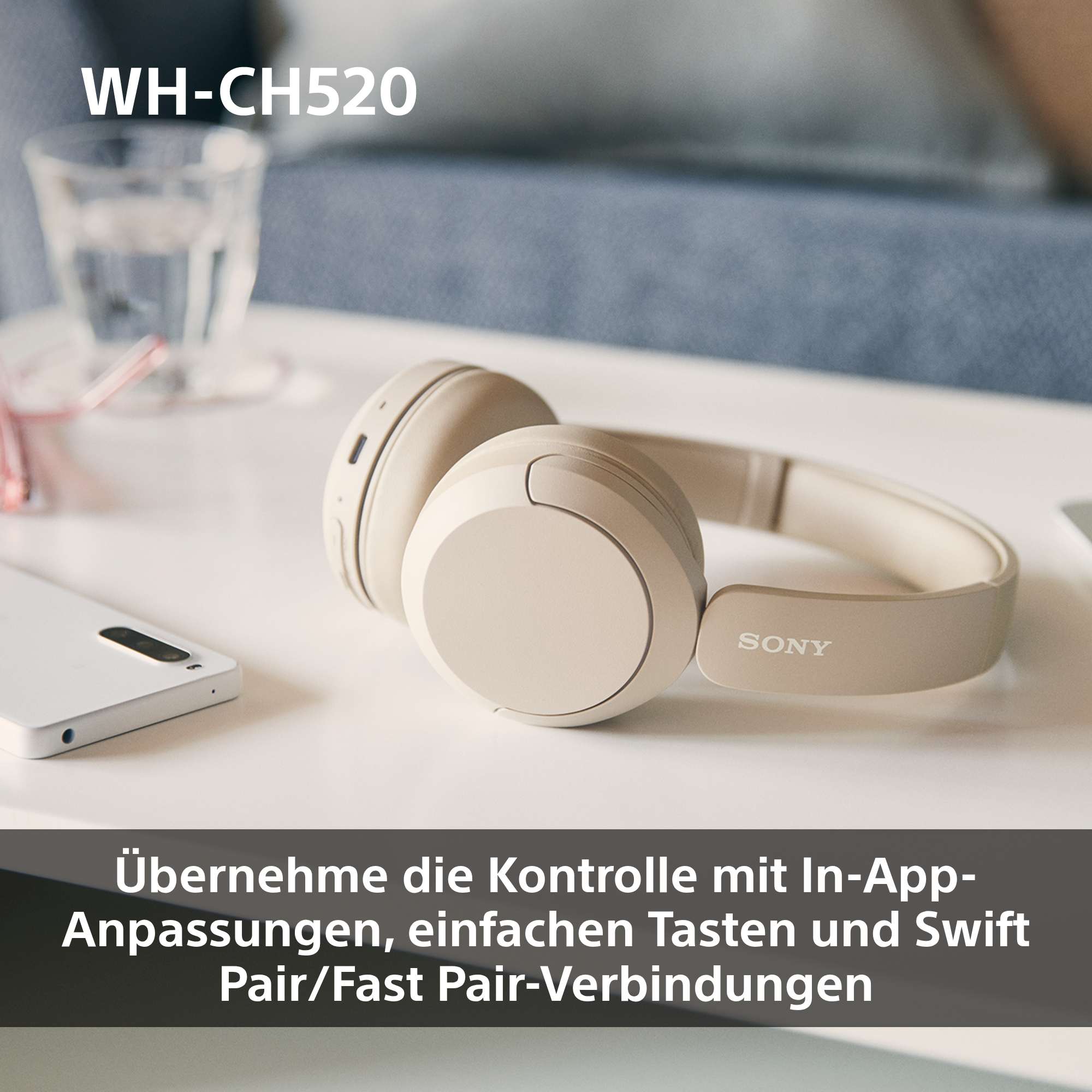 Ein Paar beige kabellose Kopfhörer auf einem weißen Tisch neben einem Smartphone.
