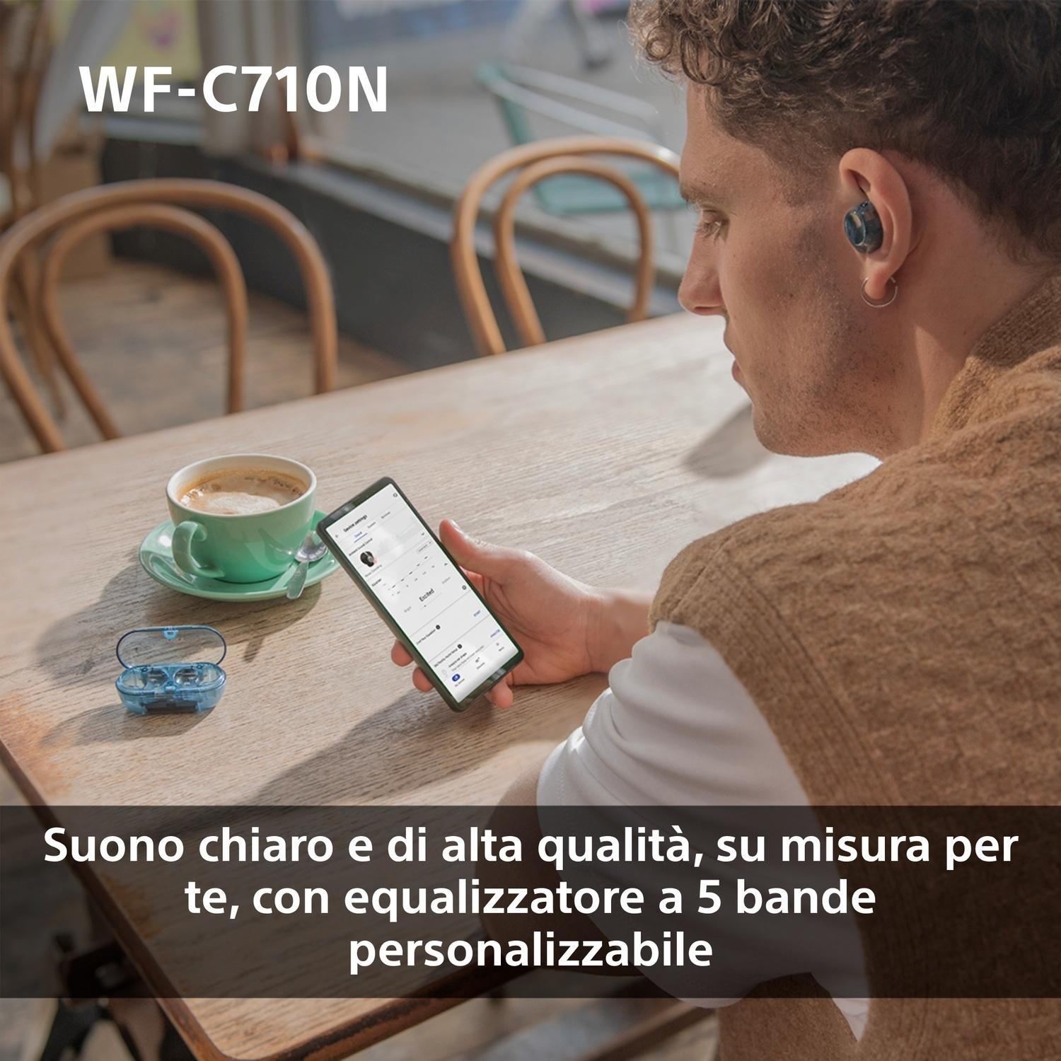 Un uomo usa un telefono e indossa auricolari wireless blu. Una tazza di caffè è sul tavolo.