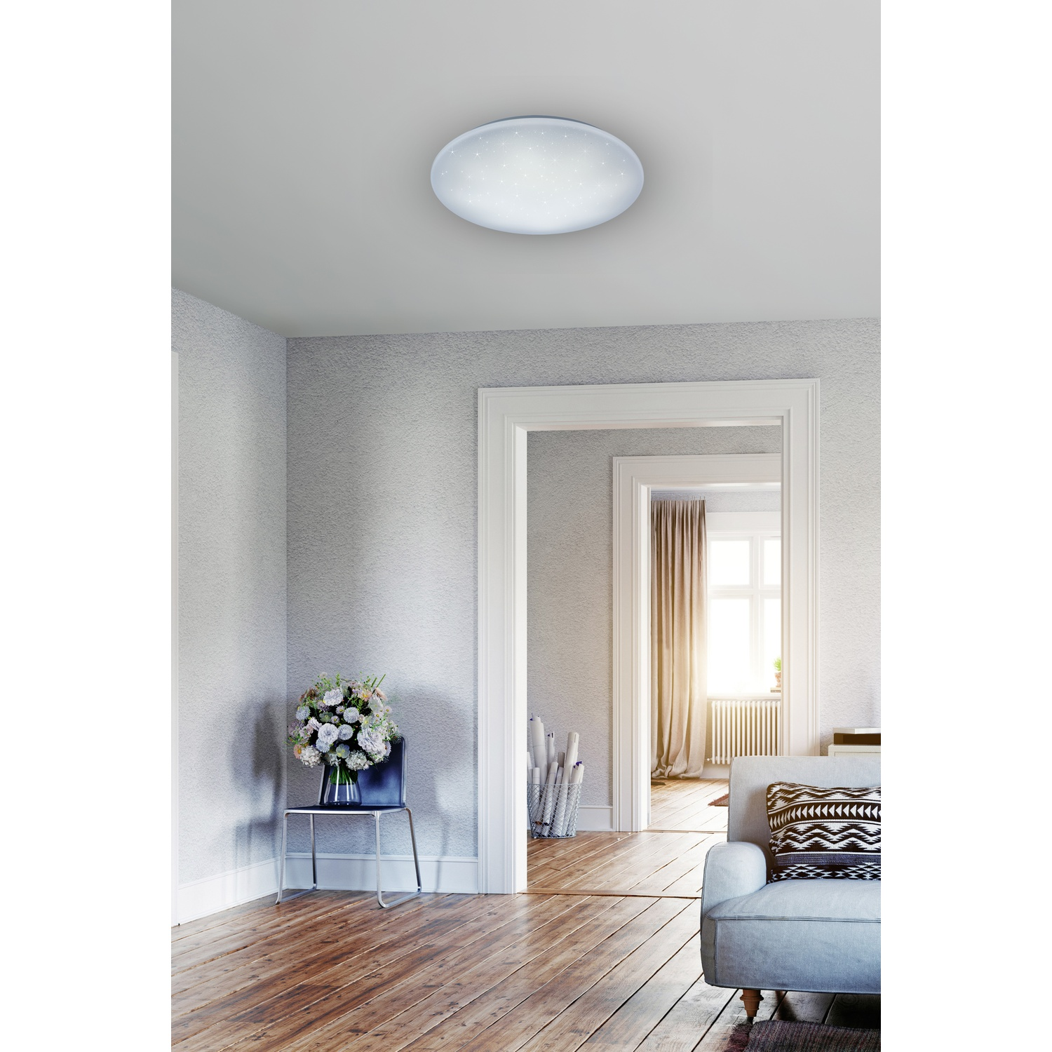 Un interno di una stanza con una luce a soffitto, una sedia, un divano e una porta verso un'altra stanza.