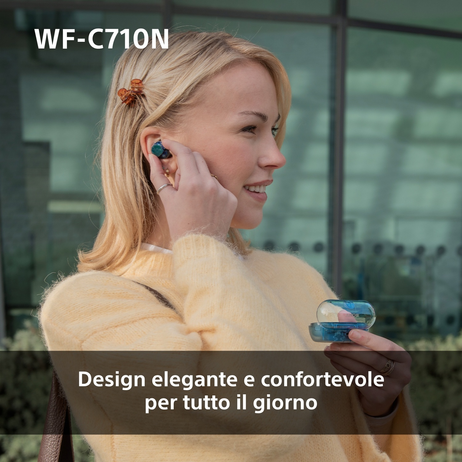 Donna con auricolari, tiene la custodia. Bionda, maglione giallo, molletta marrone.