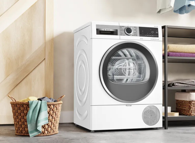 Biała pralka z koszem na ubrania po lewej stronie i półkami z ręcznikami.