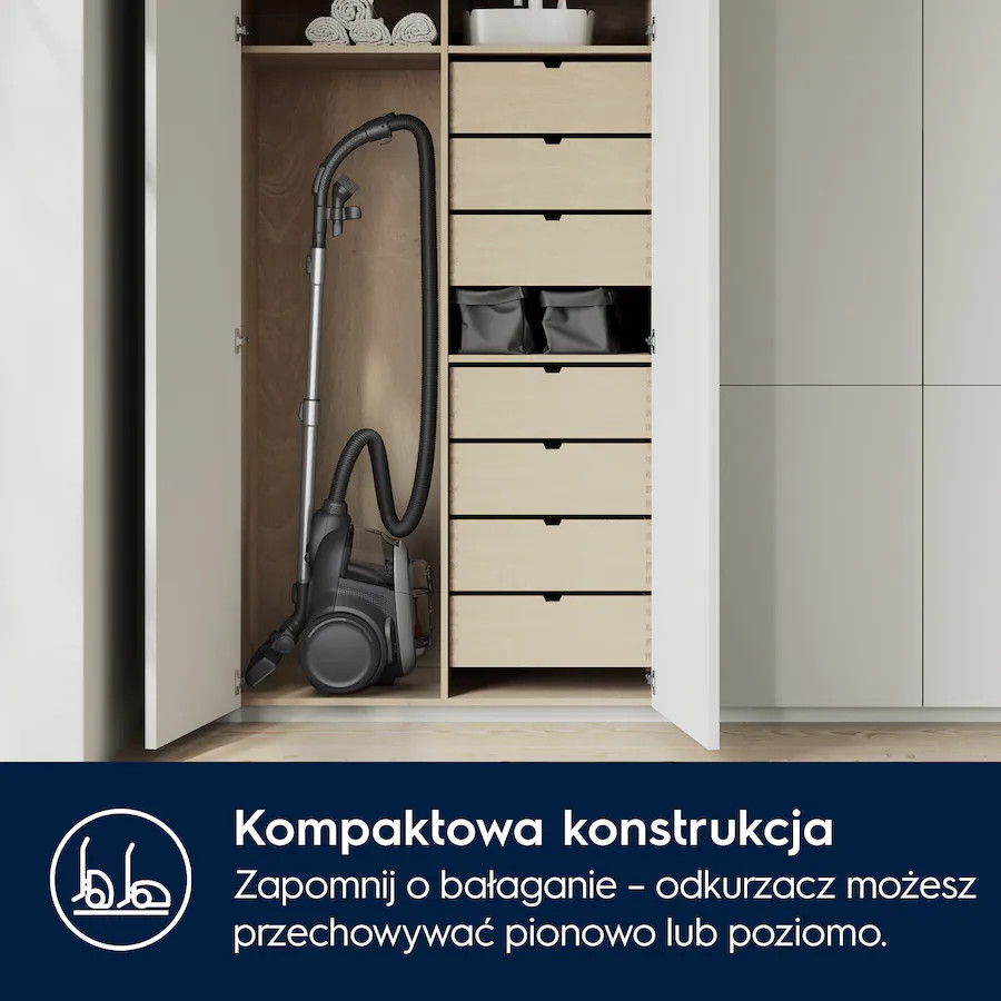 Odkurzacz wewnątrz szafki z szufladami. Otwarte drzwi szafki, białe i drewniane.