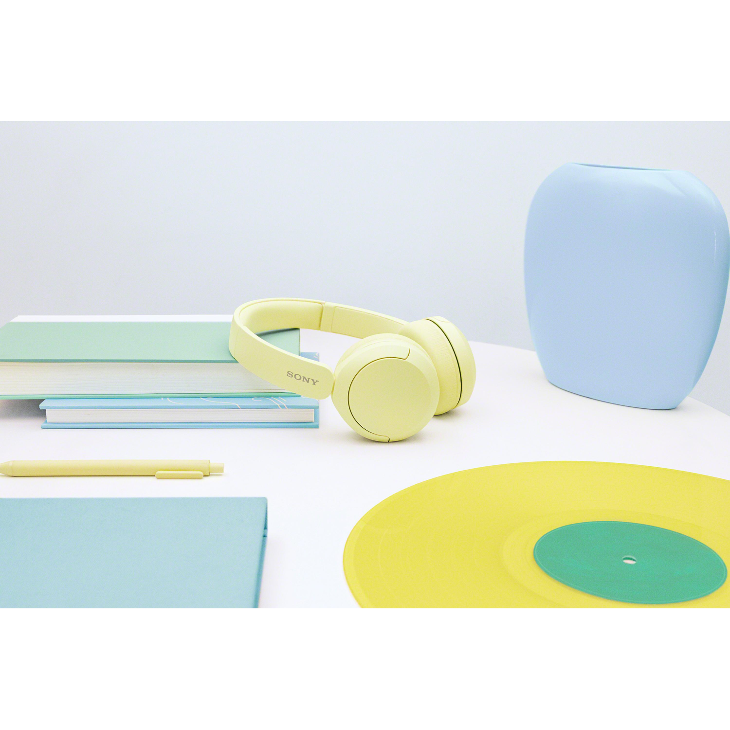 Yellow headphones, books, and a record on a white table, light blue background.