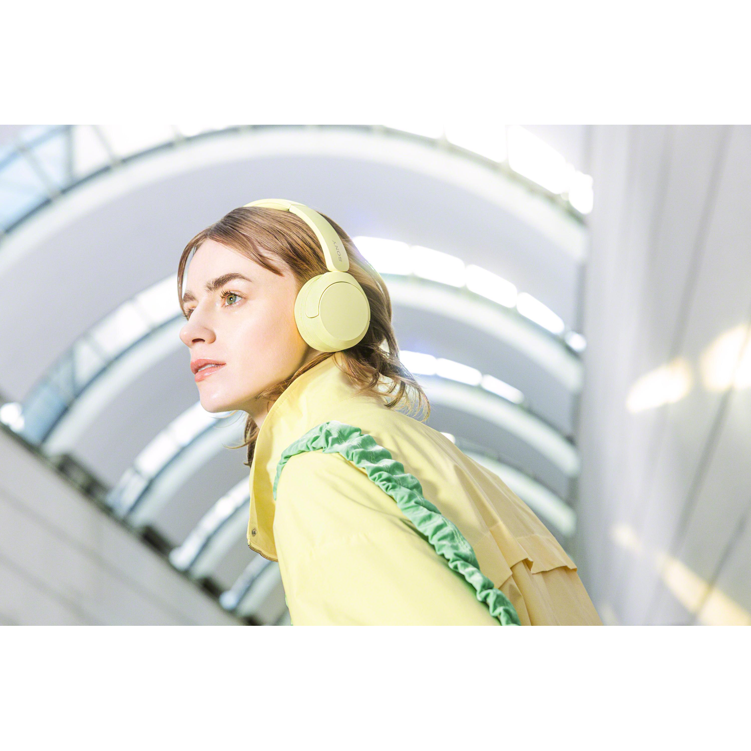 Woman wearing yellow headphones, looking sideways, with a blurred background.