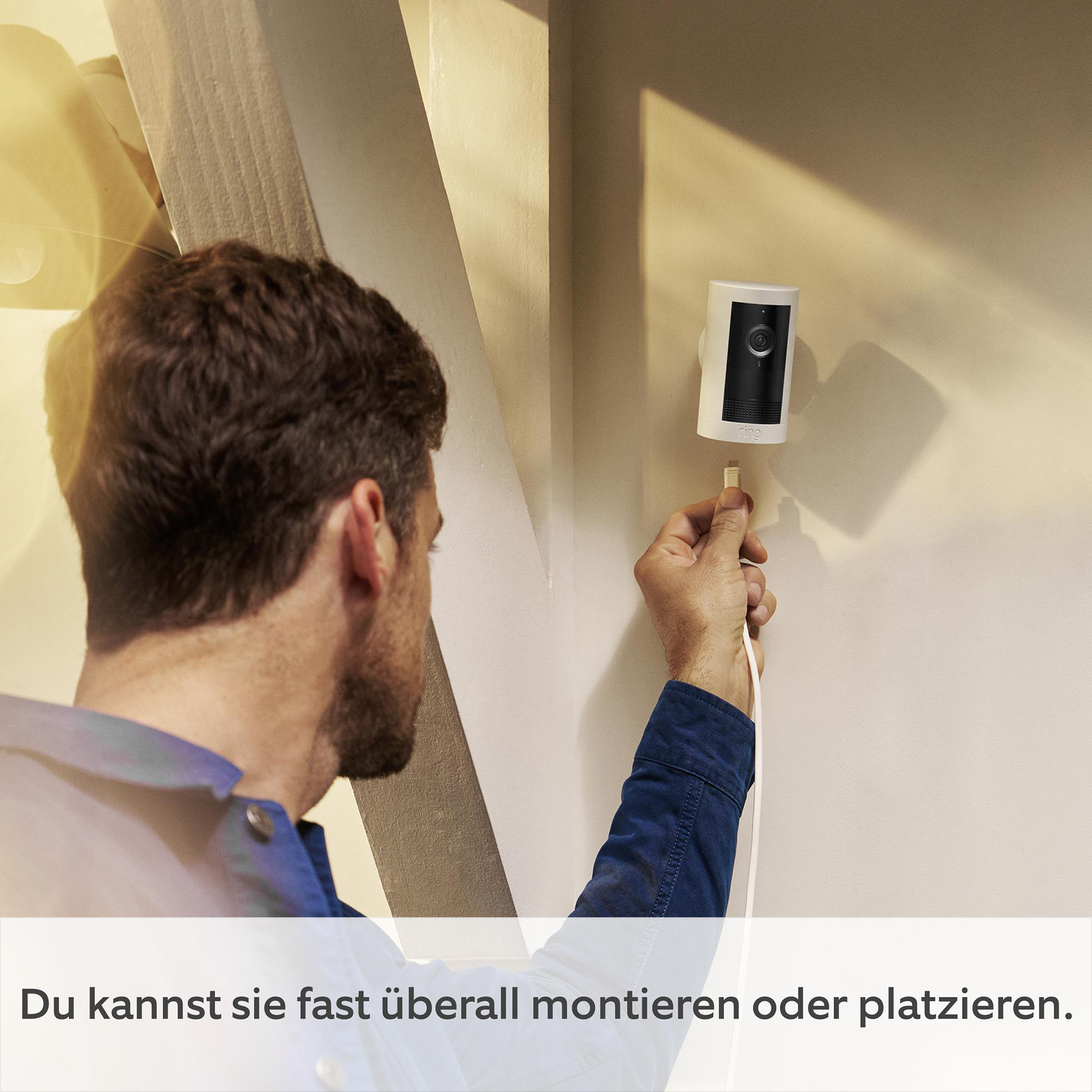 Ein Mann installiert eine weiße Überwachungskamera an einer Wand. Die Kamera hat ein schwarzes Objektiv.