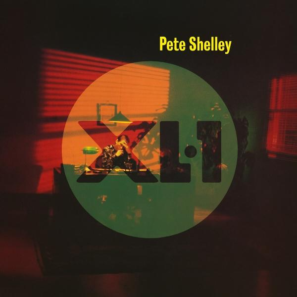 Pete Shelley Albumcover. Grünes und rotes Design, Mann im Zentrum. Dunkler Raum.