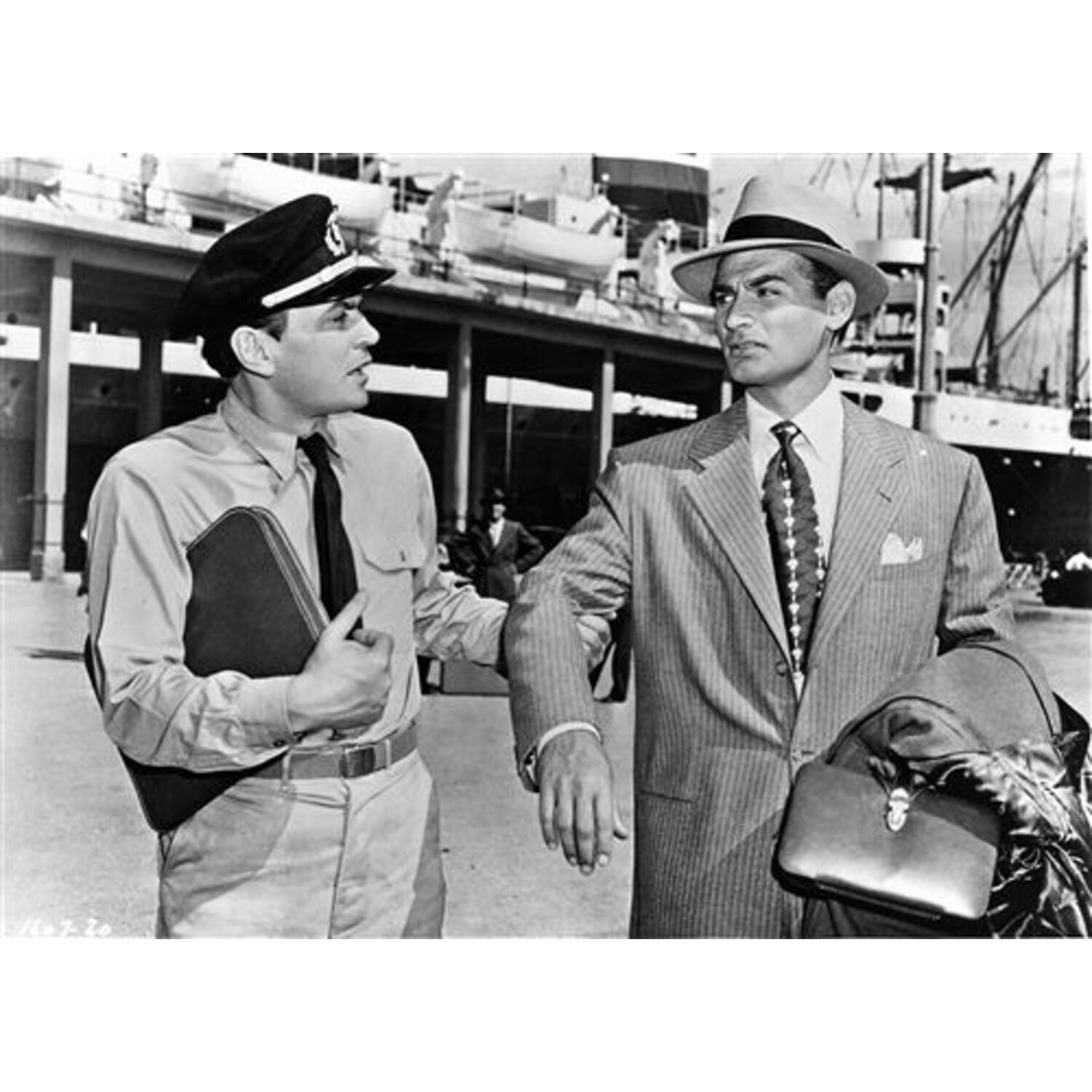 Photo en noir et blanc de deux hommes sur un quai. L'un est en uniforme, l'autre en costume.