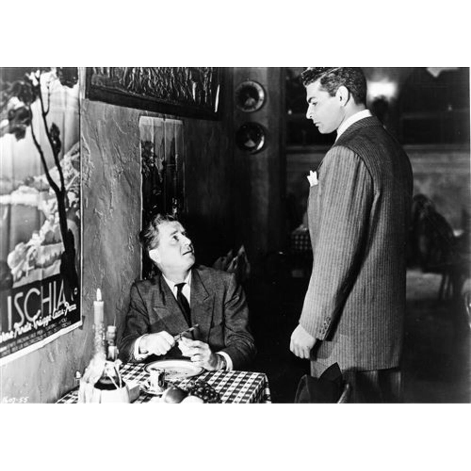 Scène de film en noir et blanc de deux hommes parlant à une table.