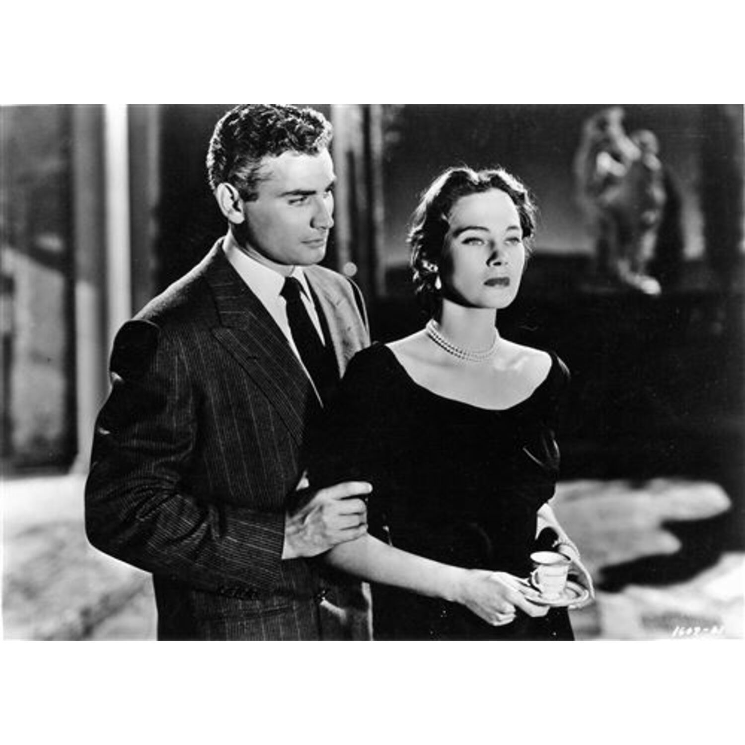 Photo en noir et blanc d'un homme en costume et d'une femme en robe. Ils sont proches.