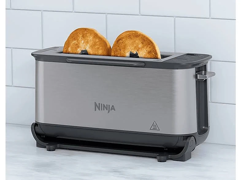 Una tostadora Ninja con dos bagels tostados. Es plateada y negra sobre un fondo de azulejos blancos. El logotipo de Ninja es visible.