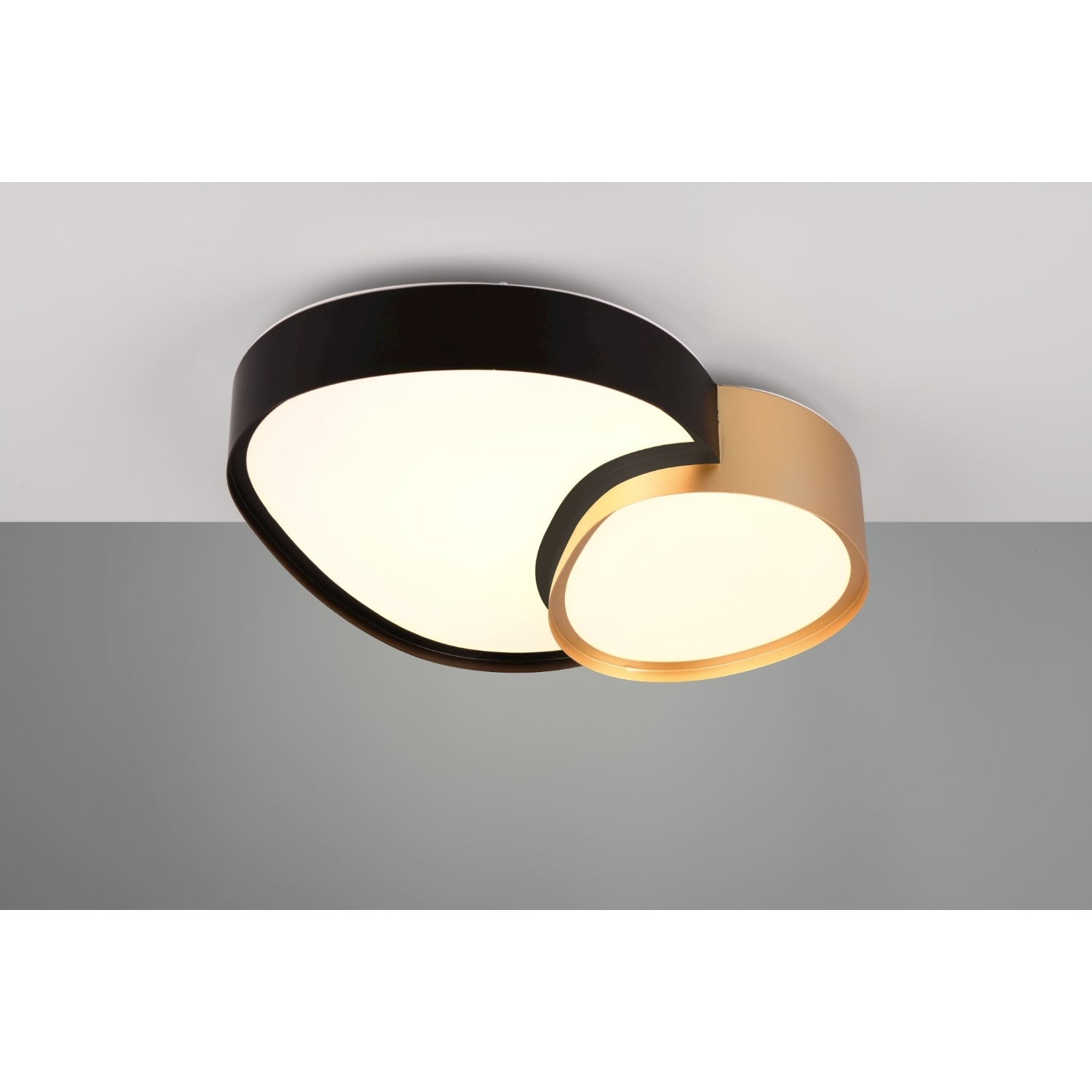 Lampada da soffitto moderna e astratta con curve nere e dorate, montata su un soffitto grigio.