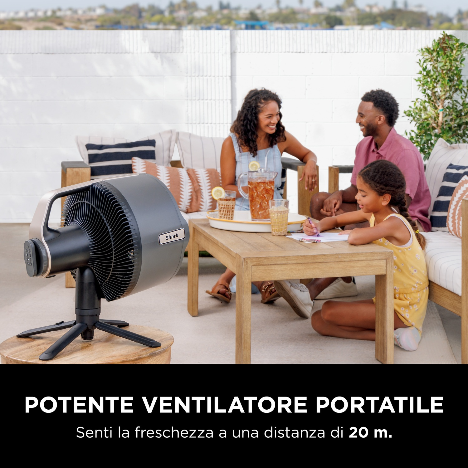 Una famiglia seduta fuori, vicino a un ventilatore, tavolo e bevande.