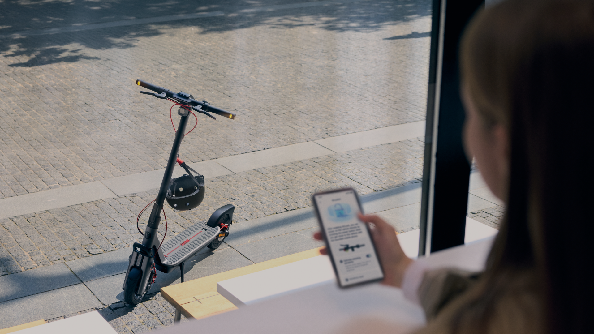 Une femme regarde son téléphone, un scooter avec un casque est dans la rue devant une vitrine.