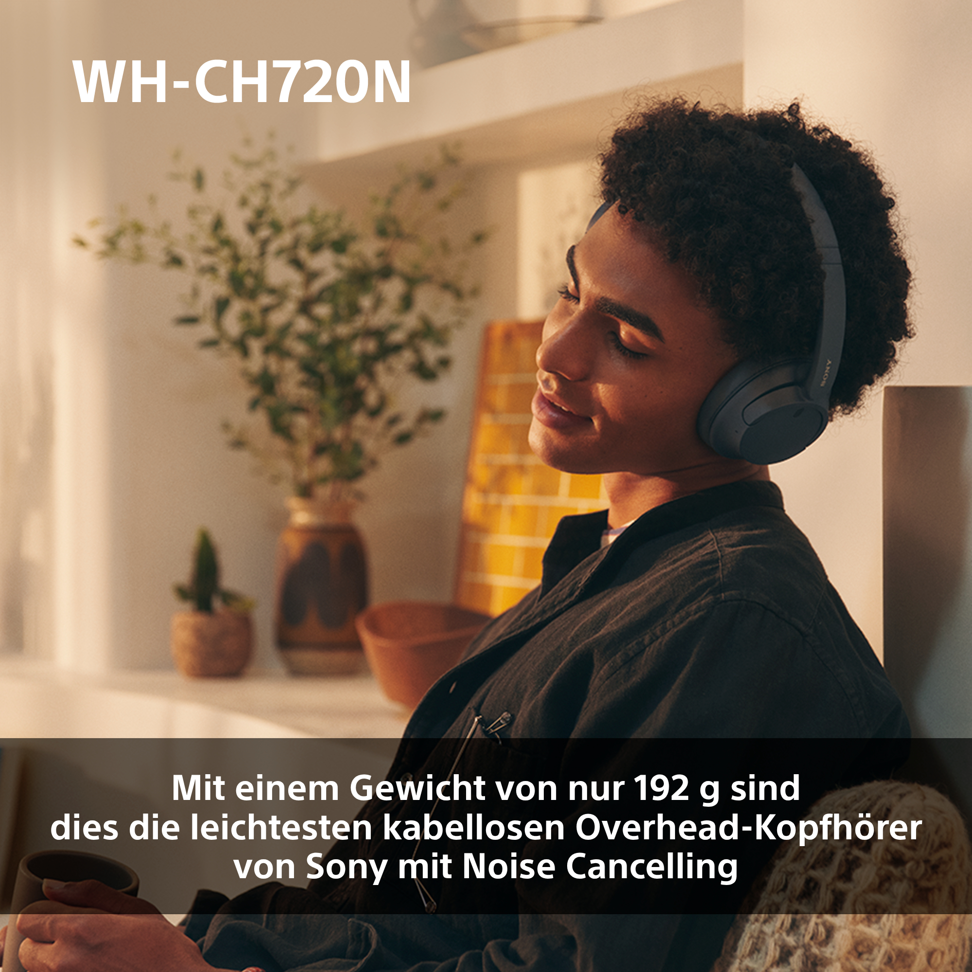 Frau mit grauen Kopfhörern in einem Raum mit Pflanzen.
