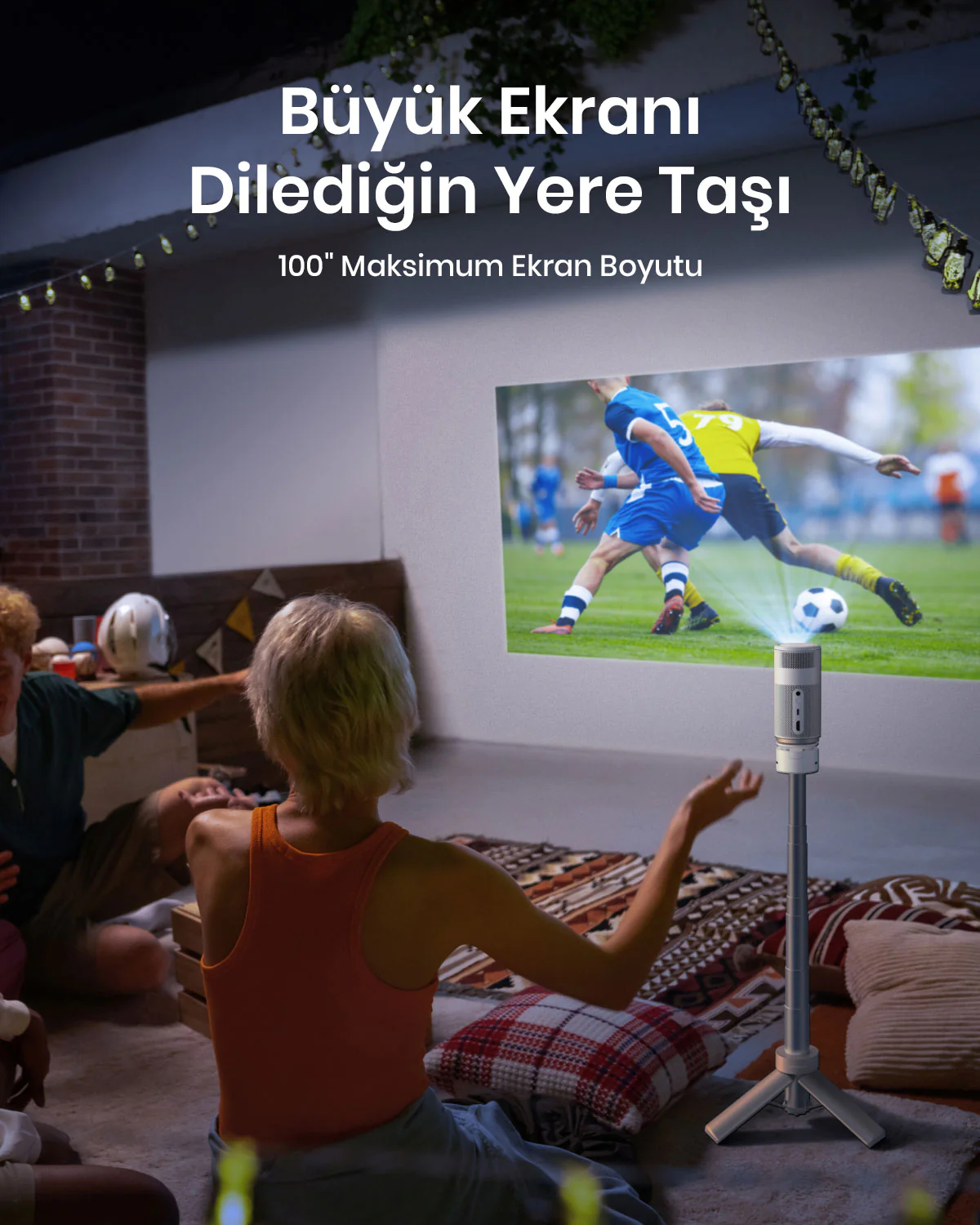 İnsanlar projeksiyonla futbol maçı izliyor. Projektör, görüntüyü bir duvara yansıtan bir stand üzerinde.