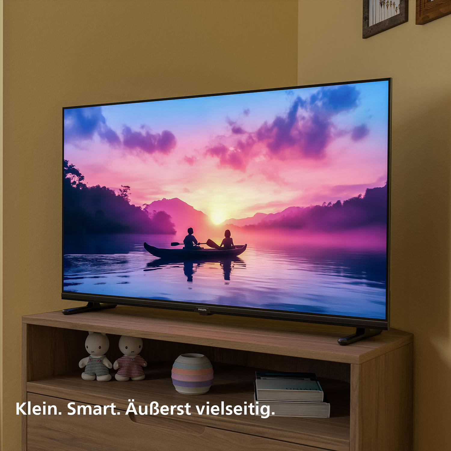 Ein Fernsehbildschirm mit Sonnenuntergang über einem See, mit einem Holzregal und Deko.