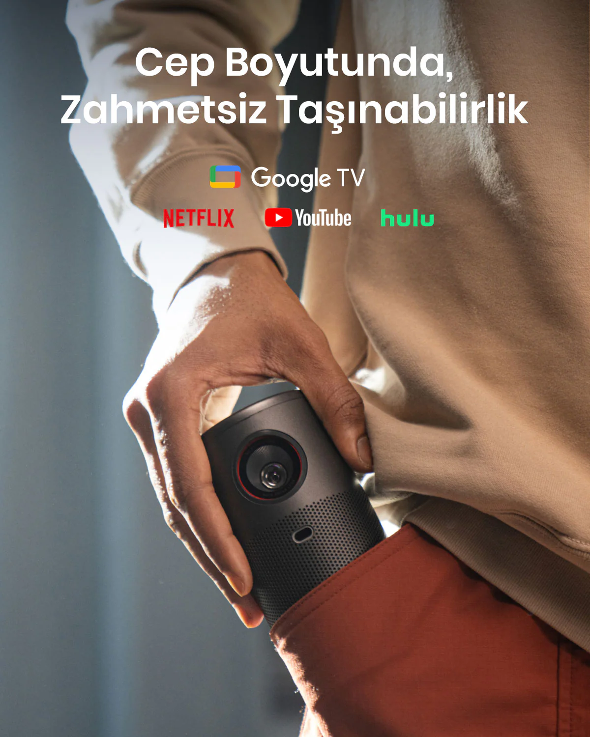 Bir kişi cebinde küçük siyah bir projektör tutuyor. Metin ve logolar görünür.