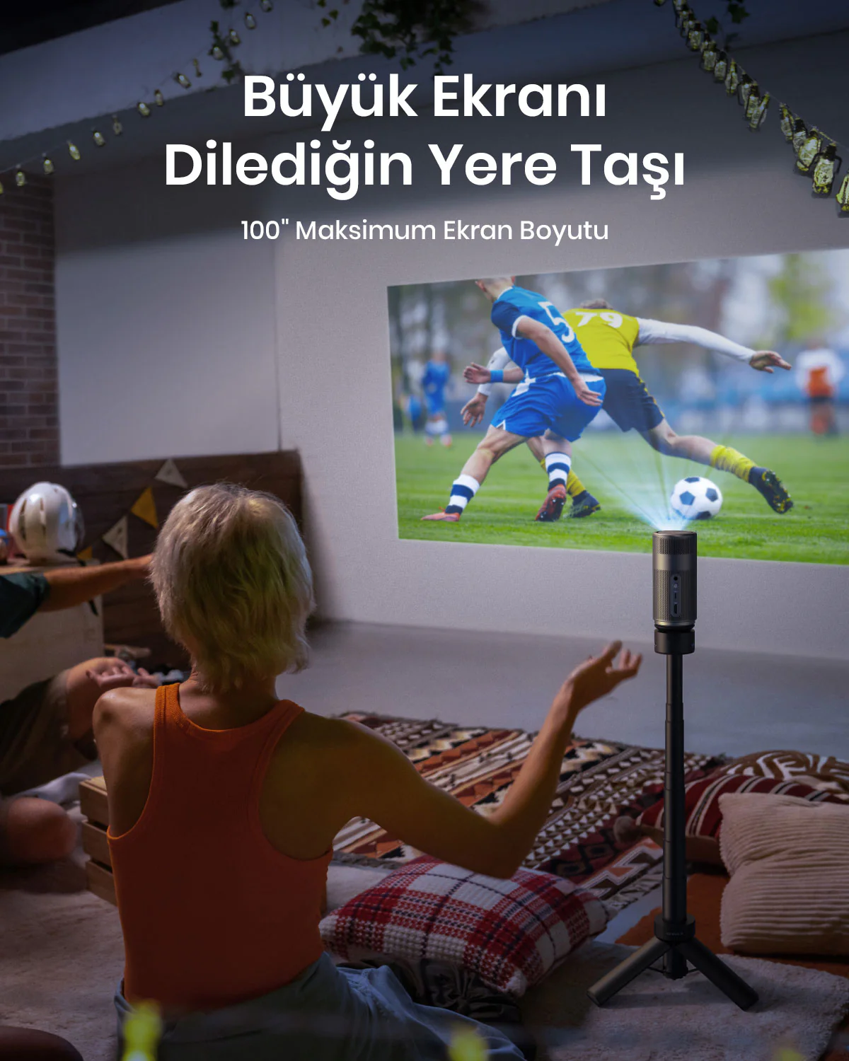 Bir kişi bir projektörde film izliyor. Projektör bir tripoda monte edilmiş. Ekran beyaz bir duvardır.