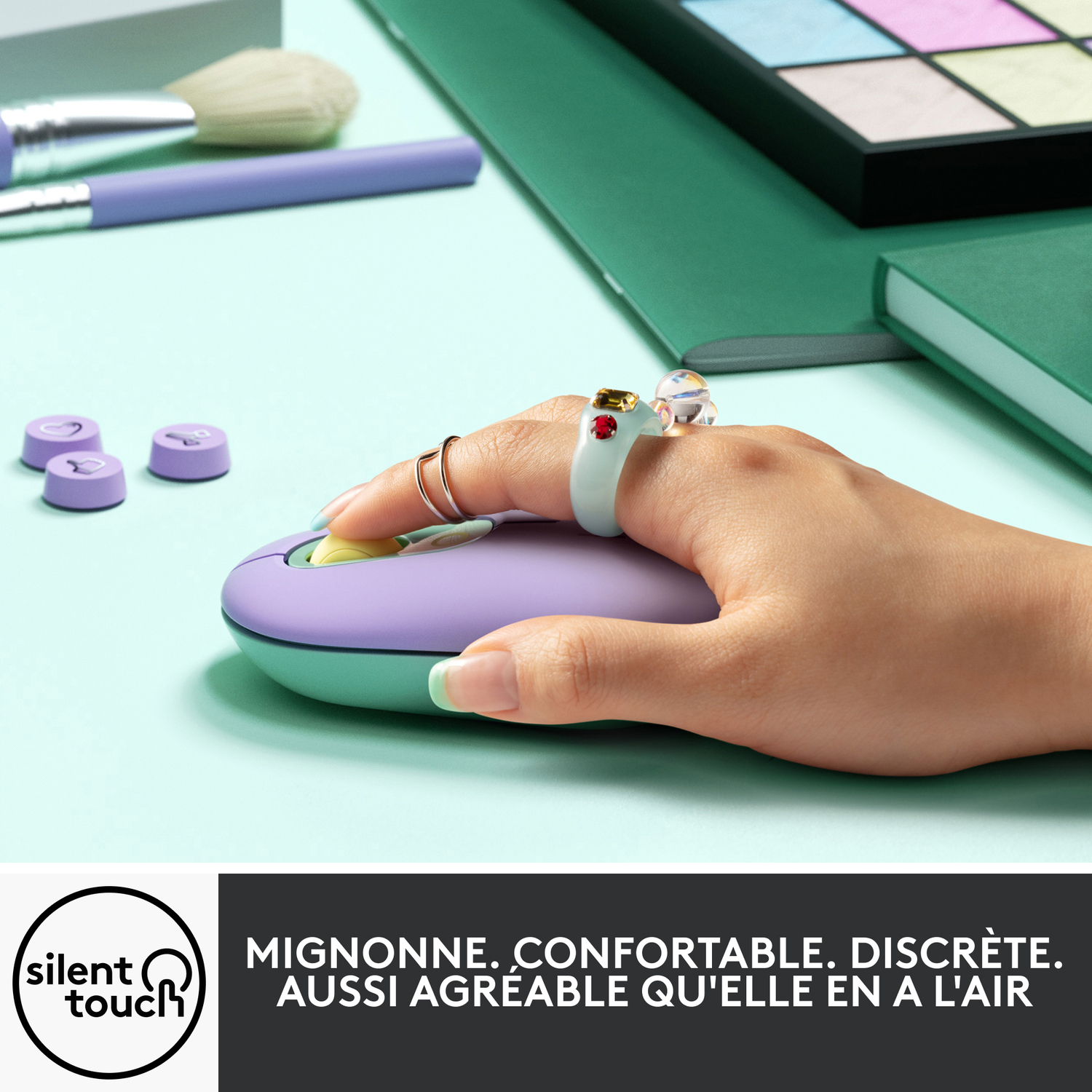 Une main portant des bagues utilise une souris violette et menthe près de maquillage et d'un journal vert.