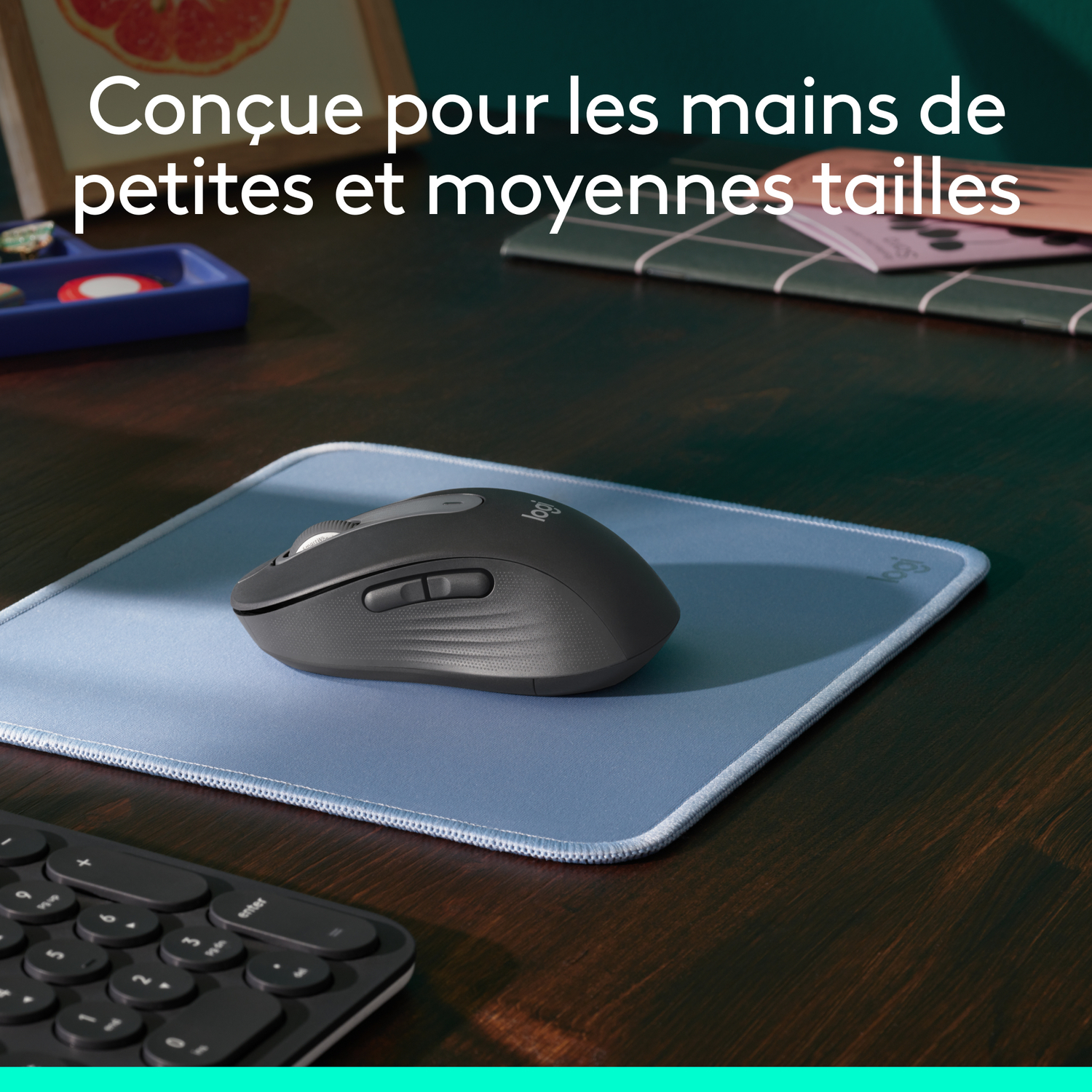 Une souris Logitech gris foncé sur un tapis de souris bleu clair sur un bureau en bois.