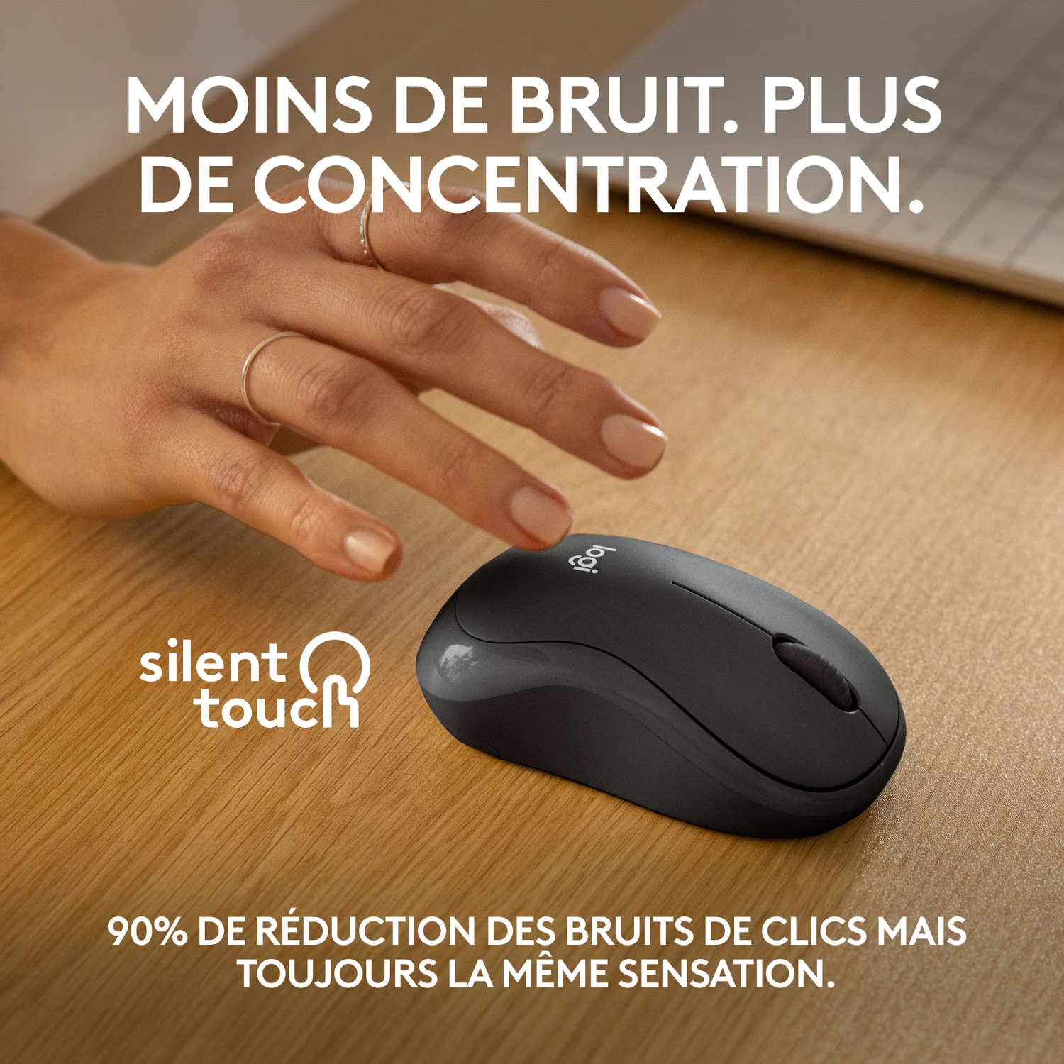 La main d'une personne touchant une souris Logitech noire sur une surface en bois.