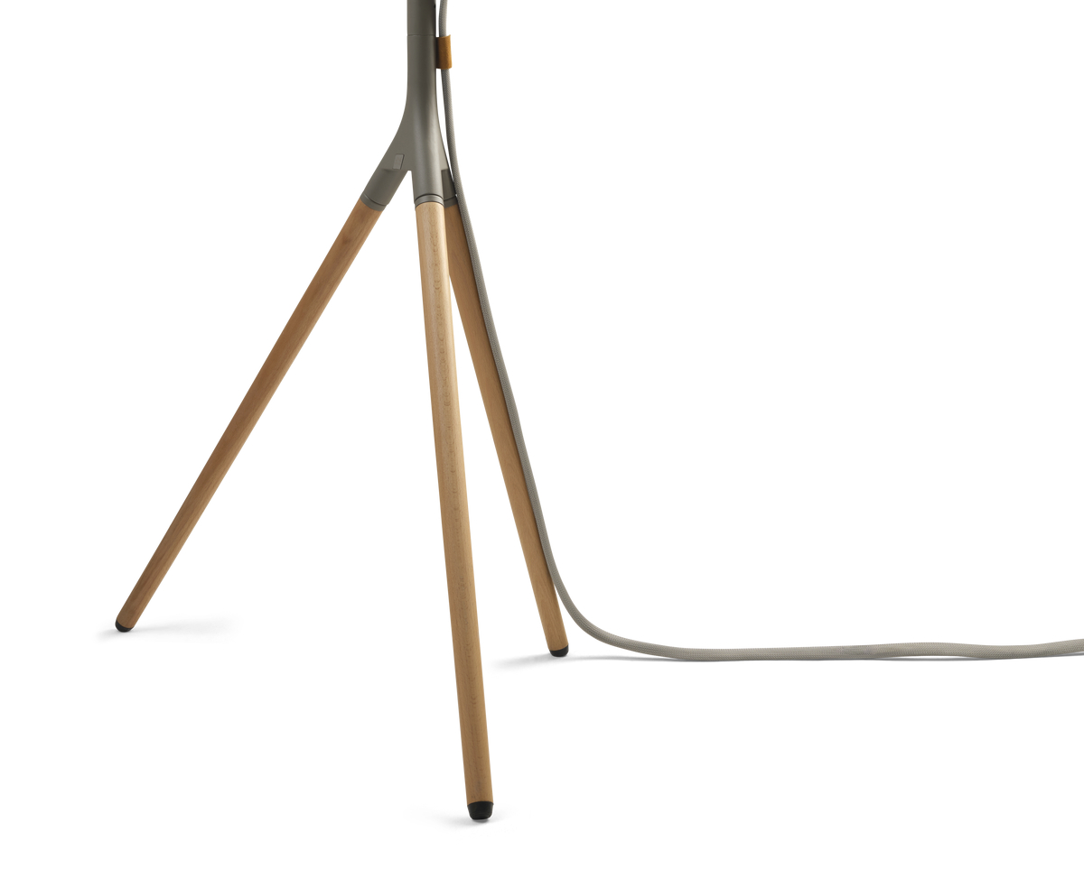 Beine einer hölzernen Stativlampe mit grauem Kabel vor weißem Hintergrund.