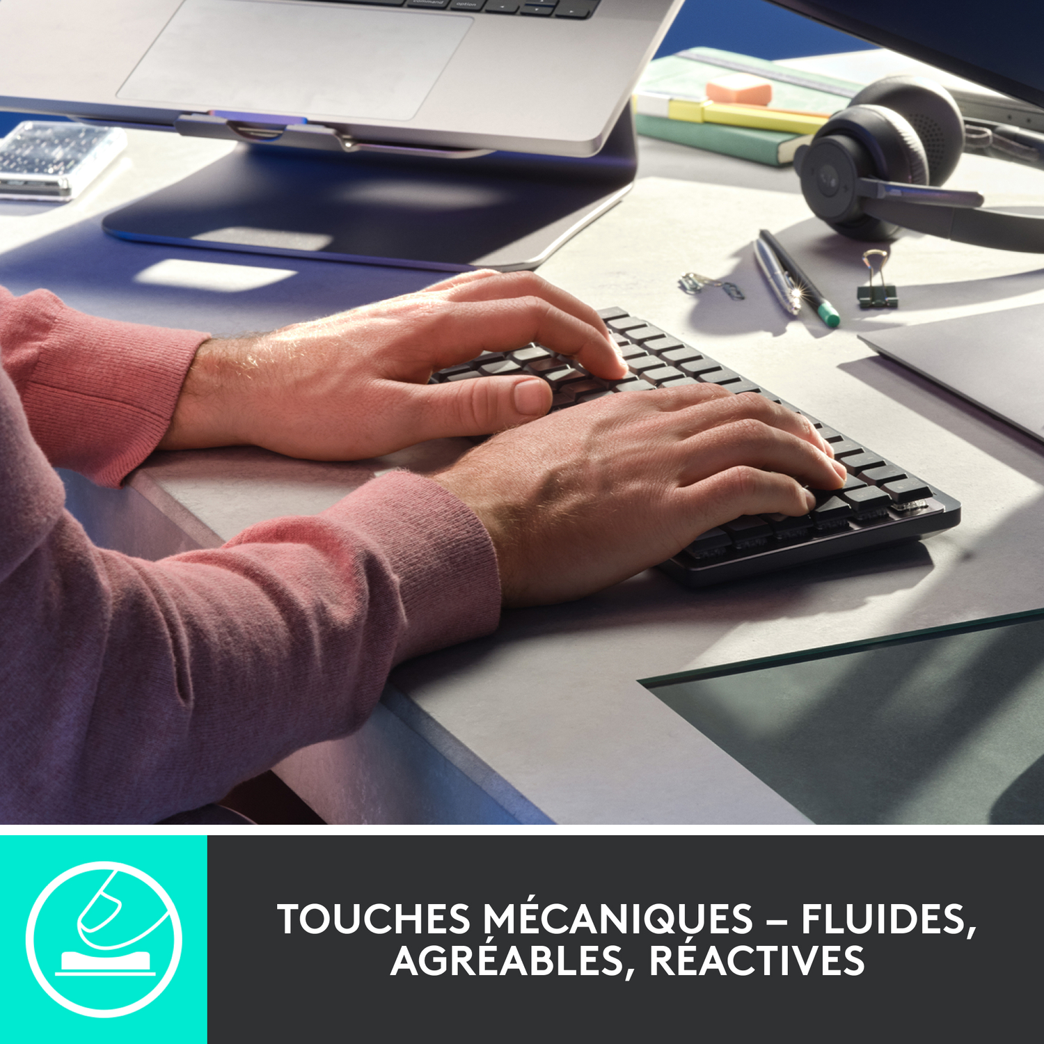 Mains tapant sur un clavier noir. Un ordinateur portable et d'autres éléments de bureau sont en arrière-plan.