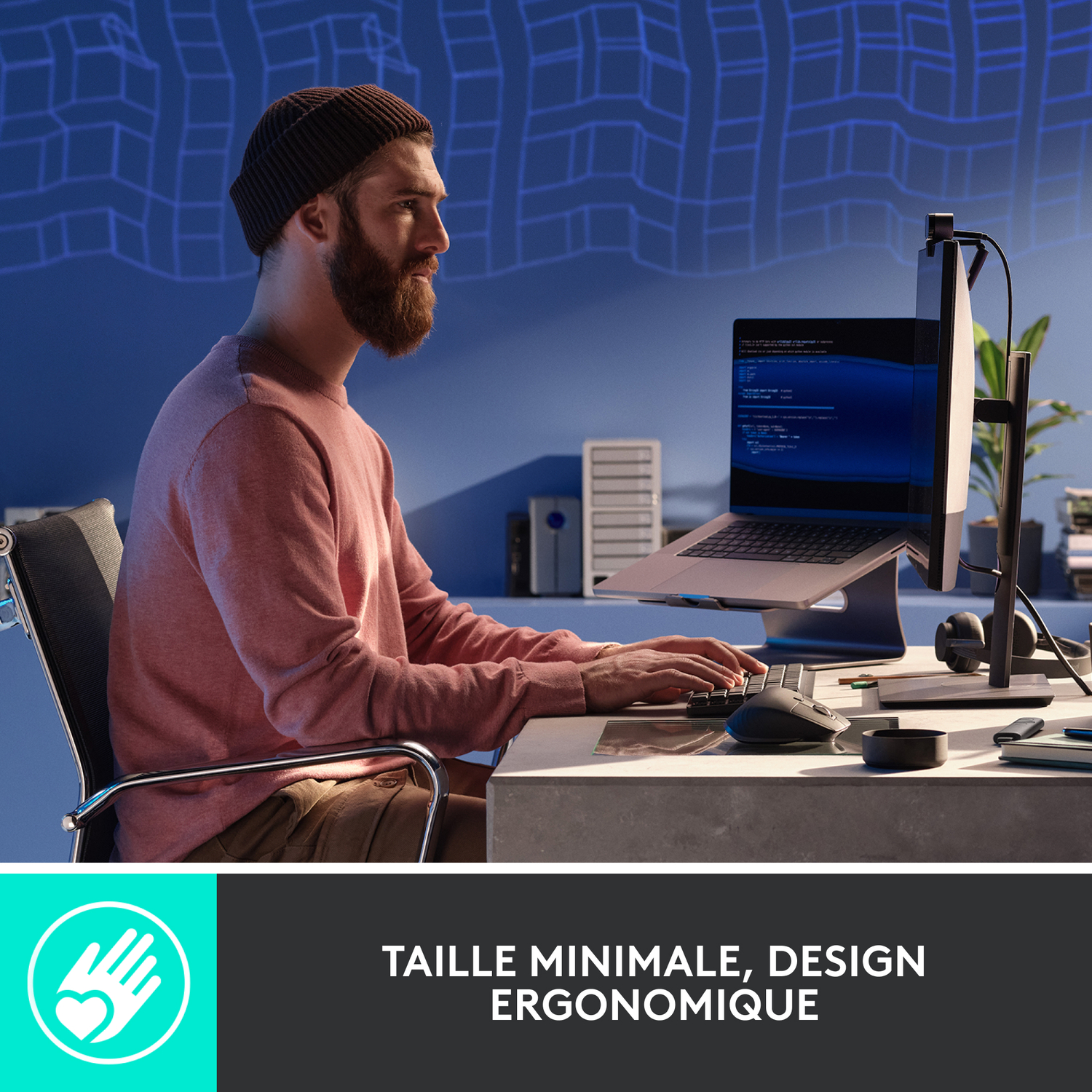 Homme travaillant sur ordinateur portable avec moniteur externe, assis à un bureau. Il porte un bonnet.