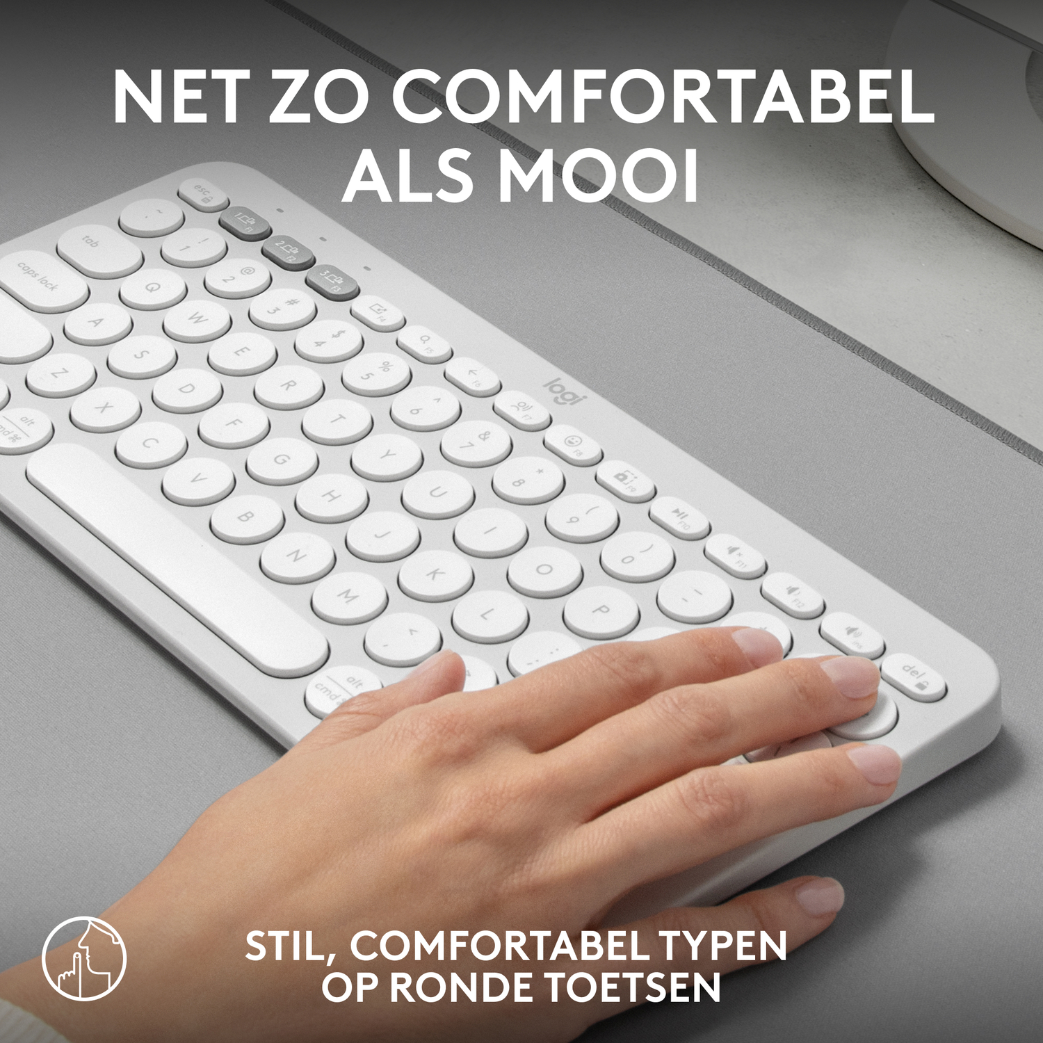 White keyboard with a hand typing on it, on a grey surface.