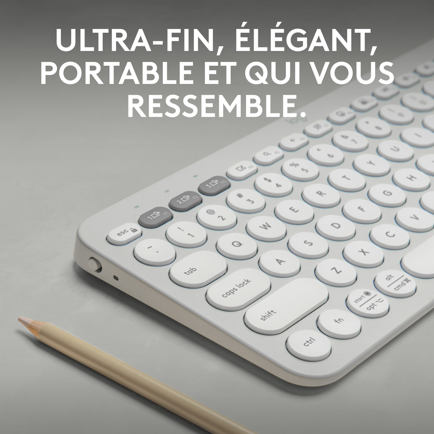 Un clavier blanc avec des touches rondes, avec un crayon. Le clavier est sur une surface grise.